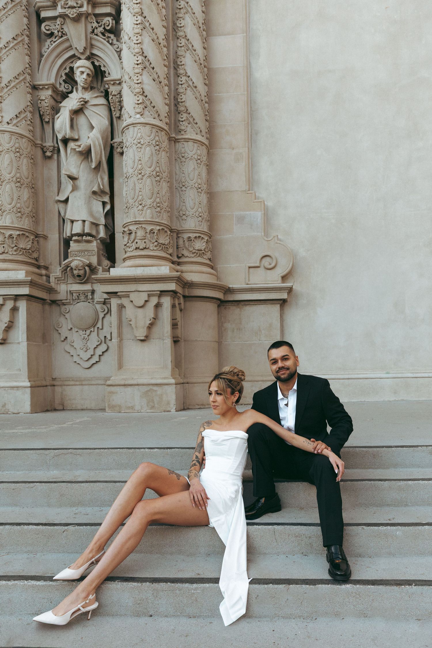 Couple in formal attire sitting on stone steps with ornate architectural details.