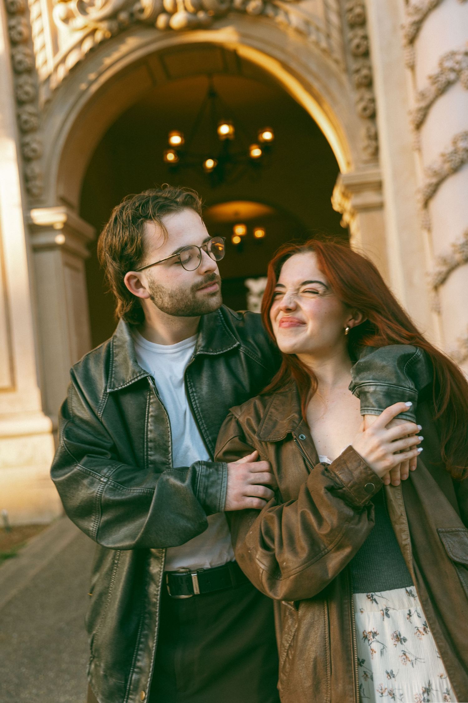 Couple sharing playful moments in front of an ornate archway with twinkling lights.