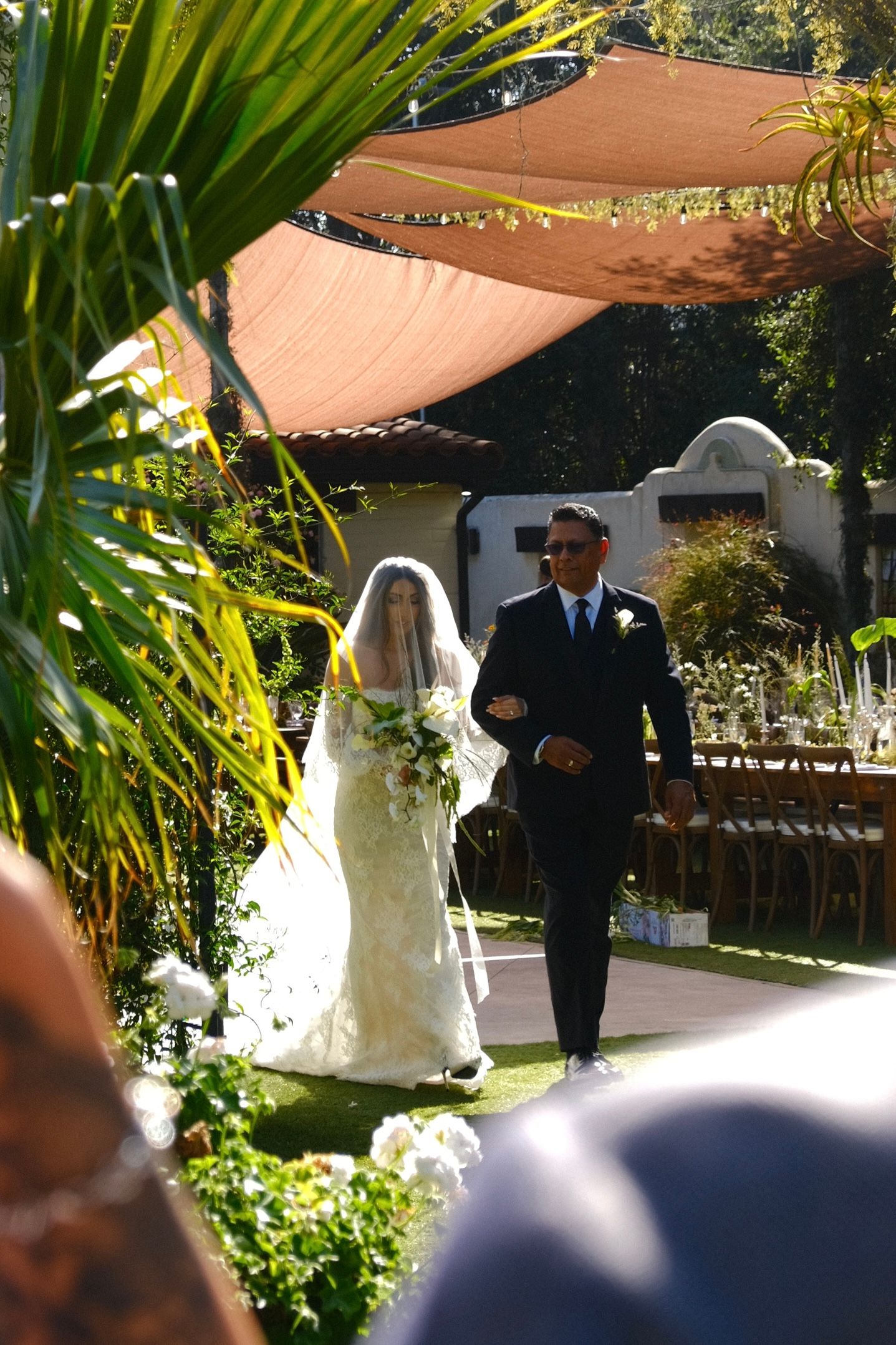 Outdoor wedding ceremony under shade sails with tropical palm fronds.