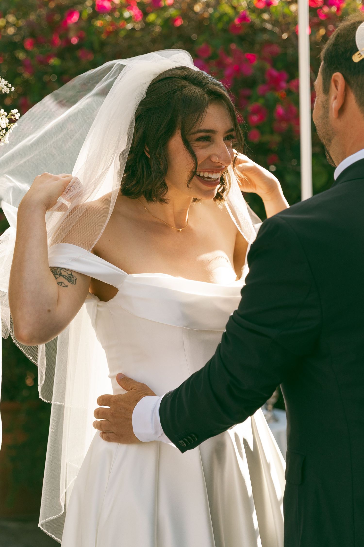 A romantic wedding moment with a bride in white dress and veil dancing outdoors among pink flowers.
