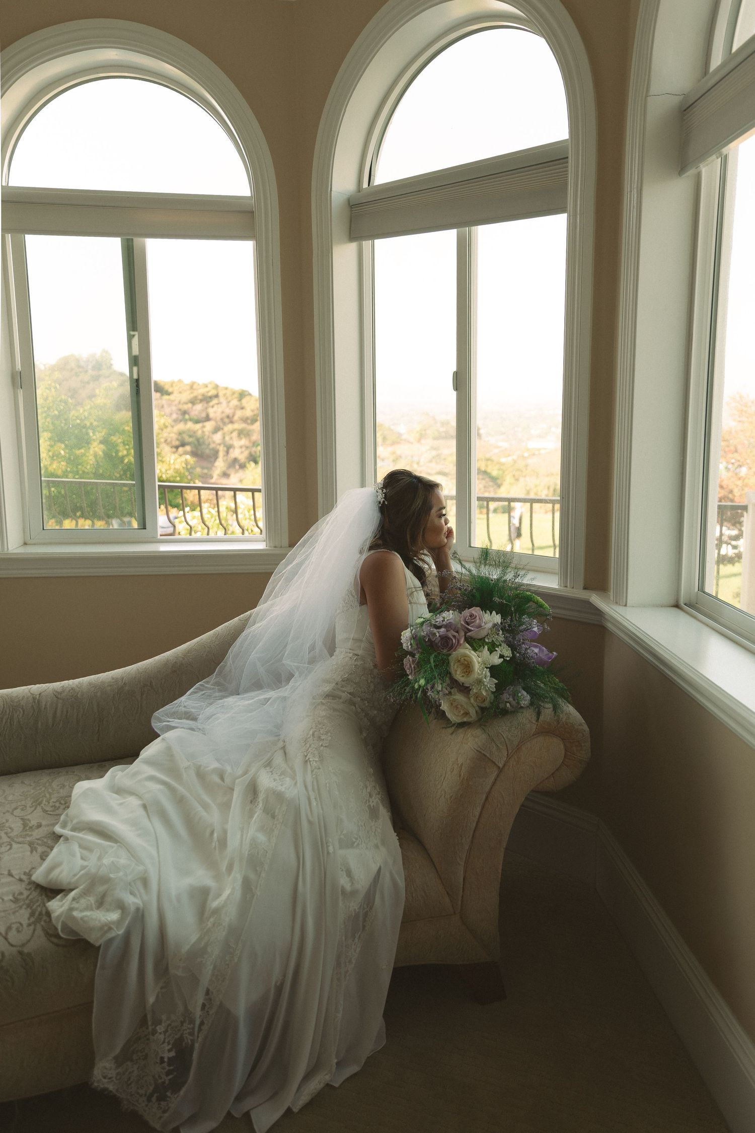 Best wedding photographer San Diego capturing a bride in her gown beside romantic arched windows in soft natural light