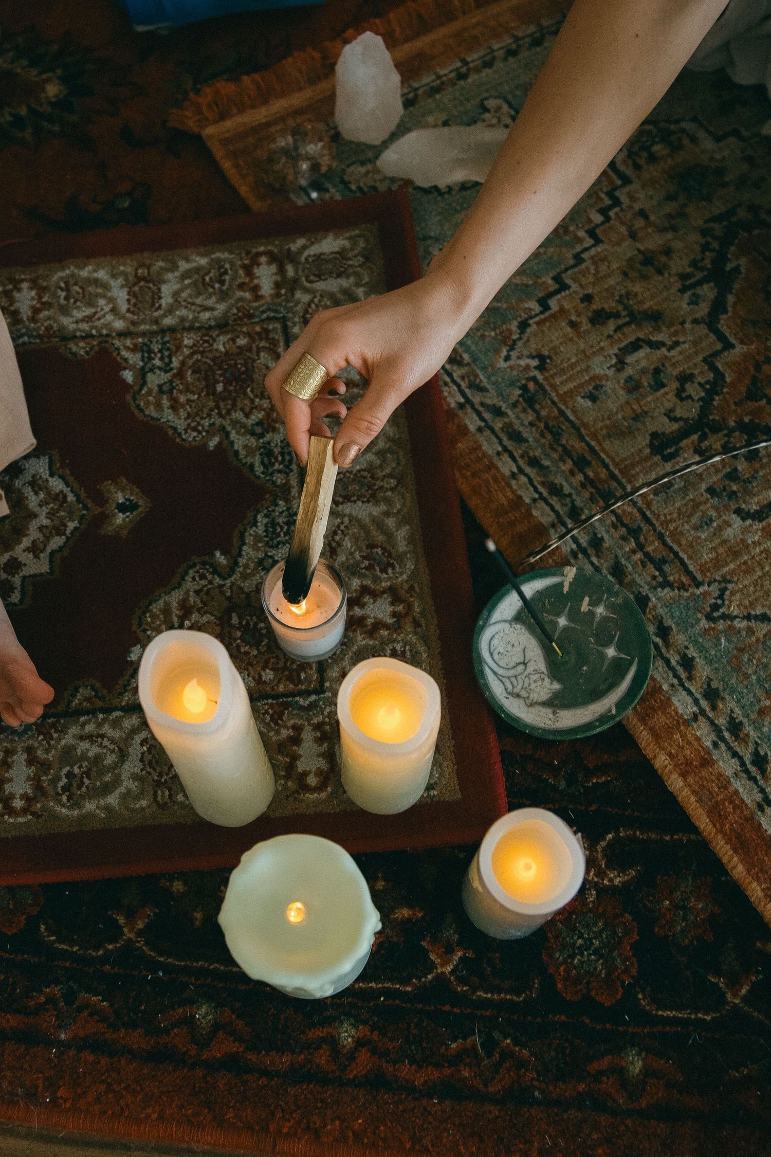 Hand lighting multiple white pillar candles on vintage patterned carpet.