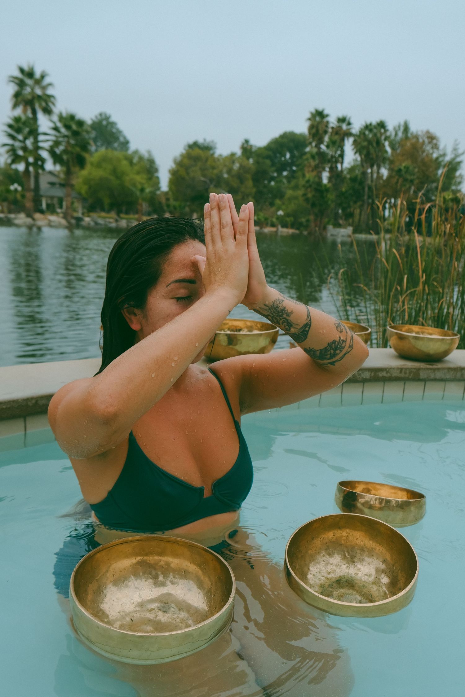 Sound healing ceremony in pool with floating copper singing bowls at sunset.