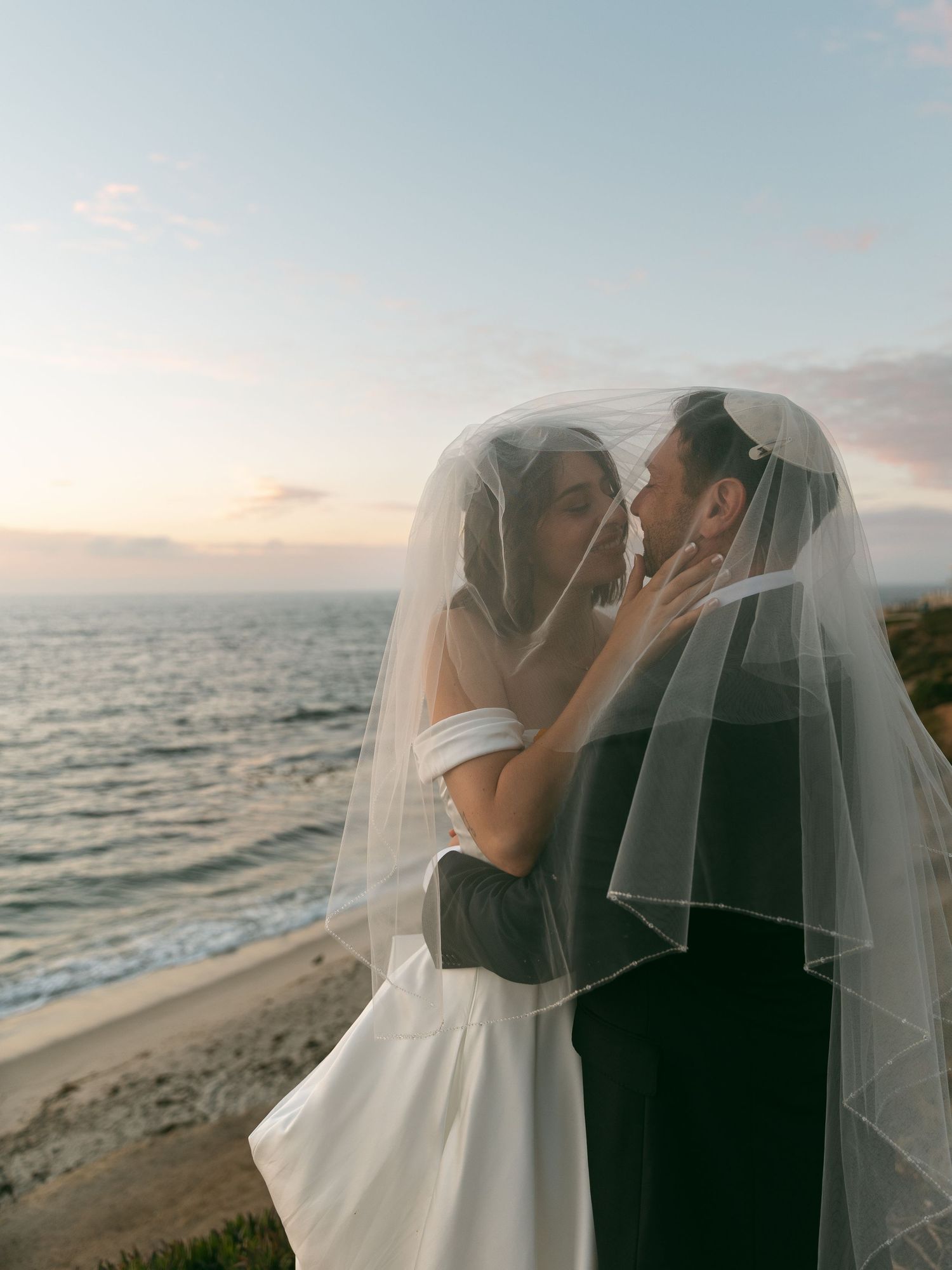 A romantic seaside wedding moment captured against the backdrop of waves and sky.