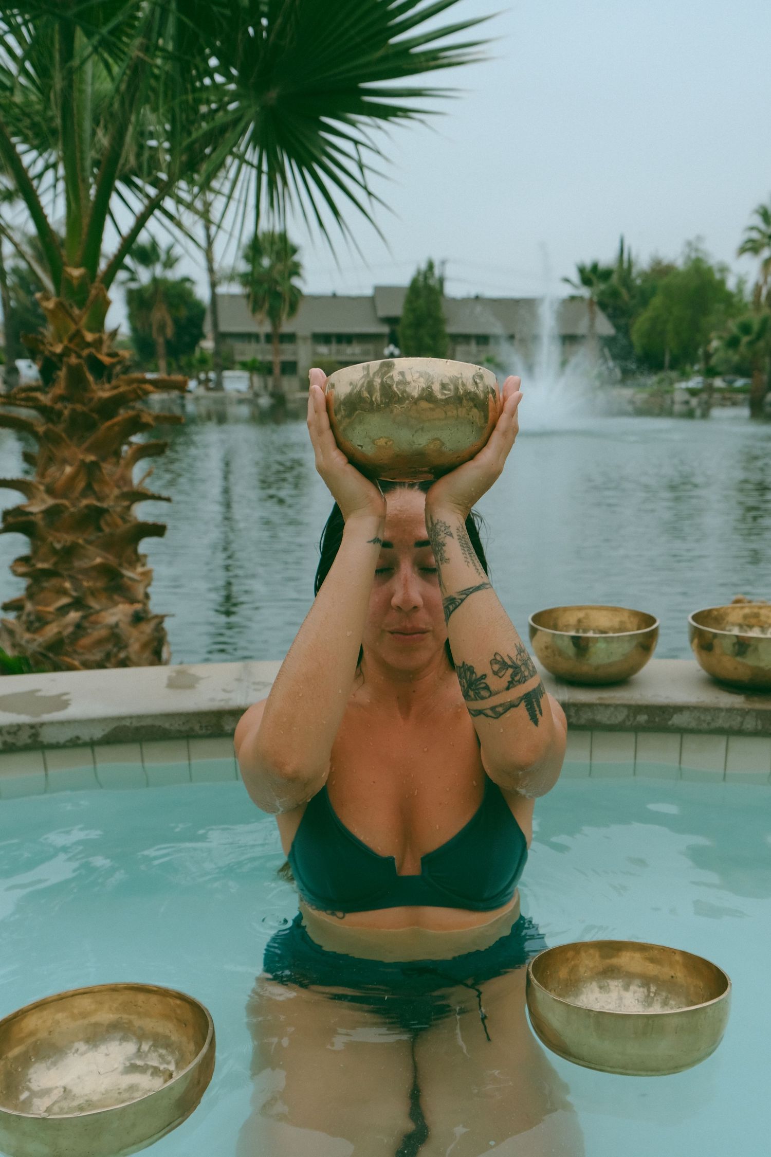 Person in black swimwear holding a golden singing bowl above their head in a pool.