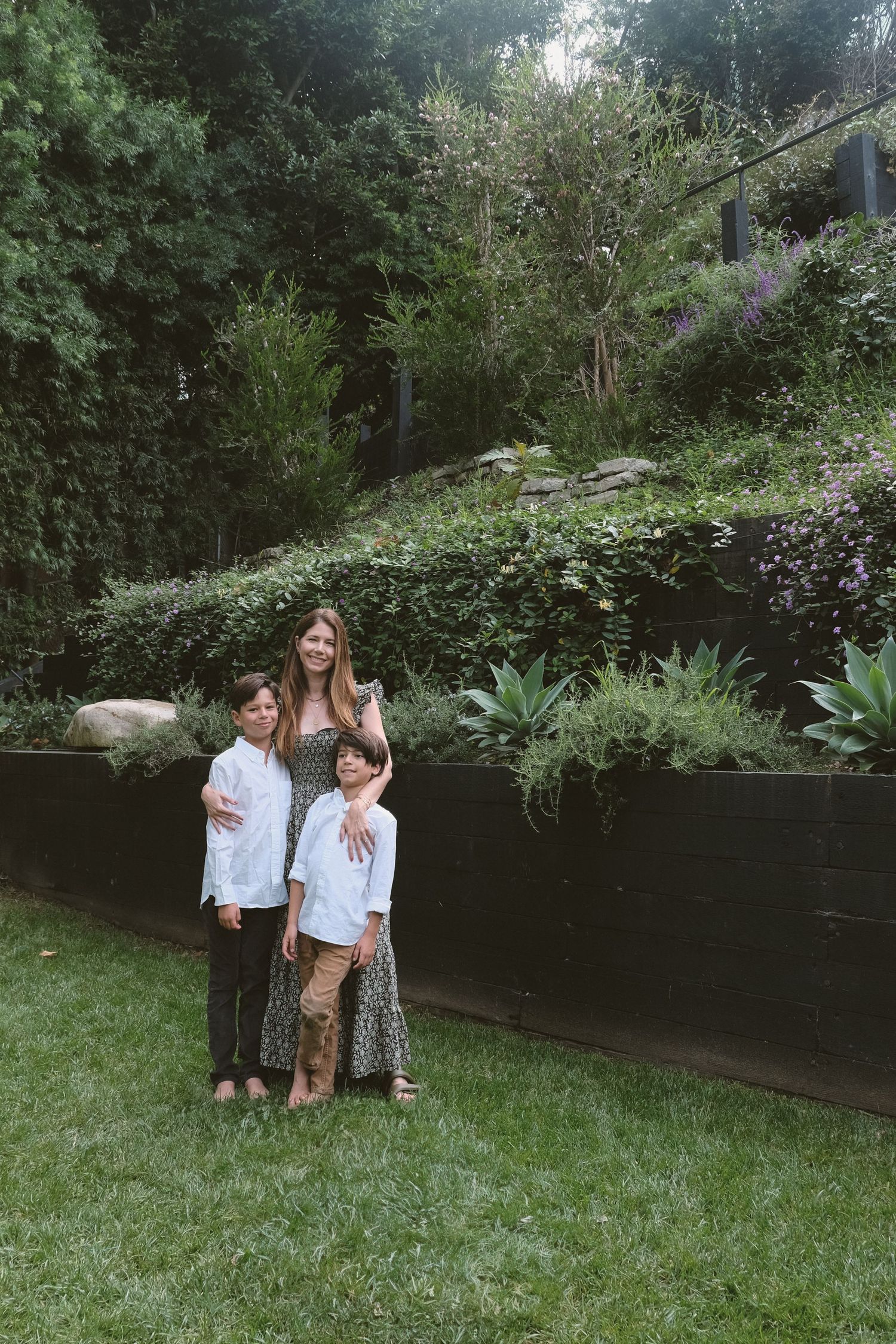 People stand together in a lush backyard garden with greenery and a black fence.