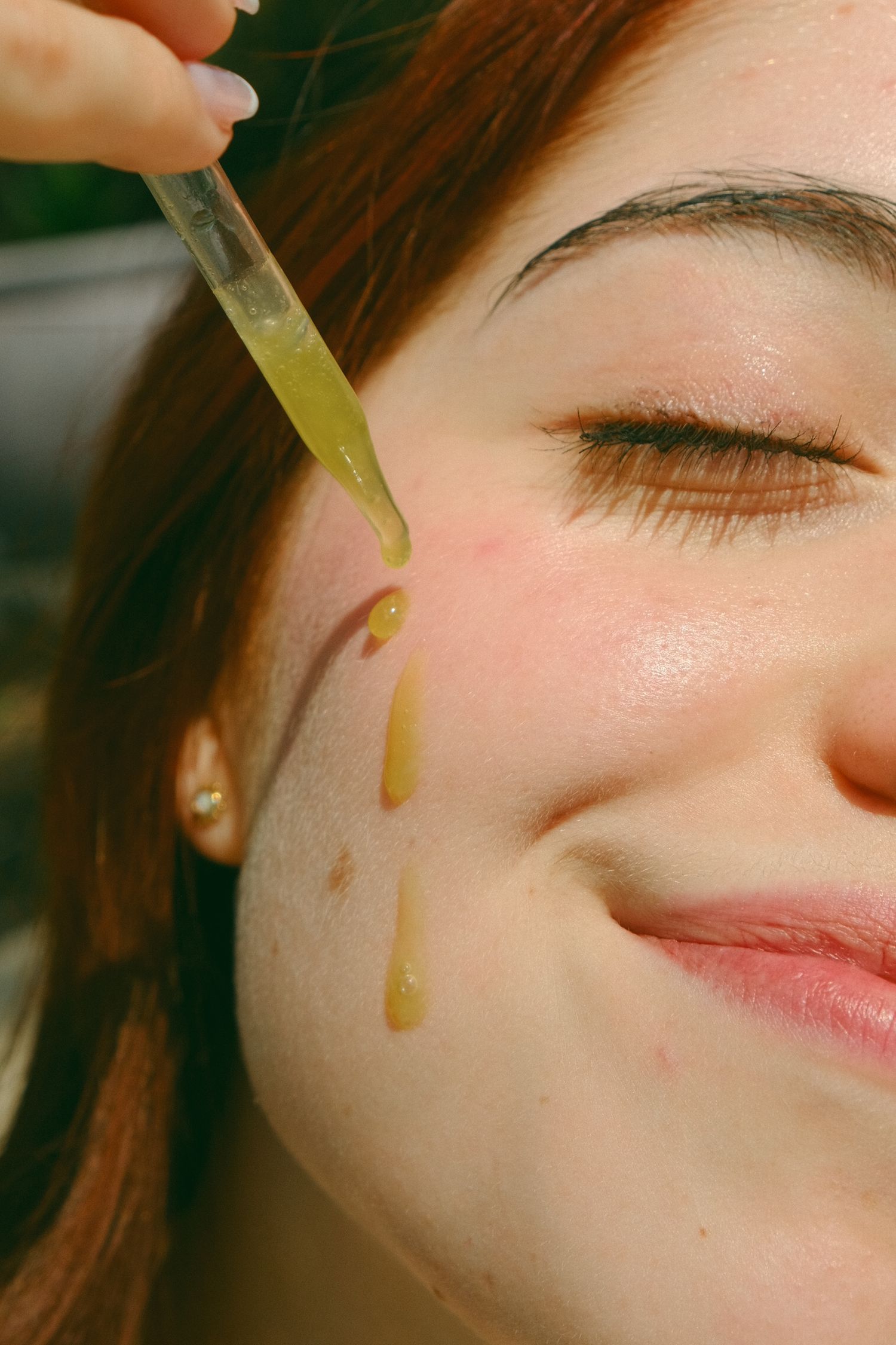 Close-up of golden serum being applied in drops to skin in natural lighting.