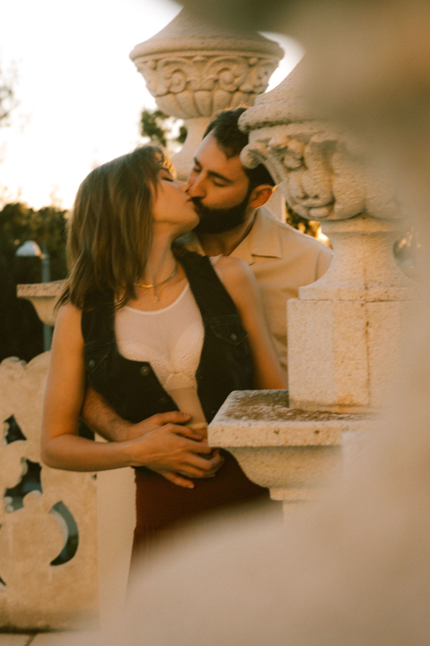 An intimate moment shared between a couple near an ornate stone column with vintage-style photography.