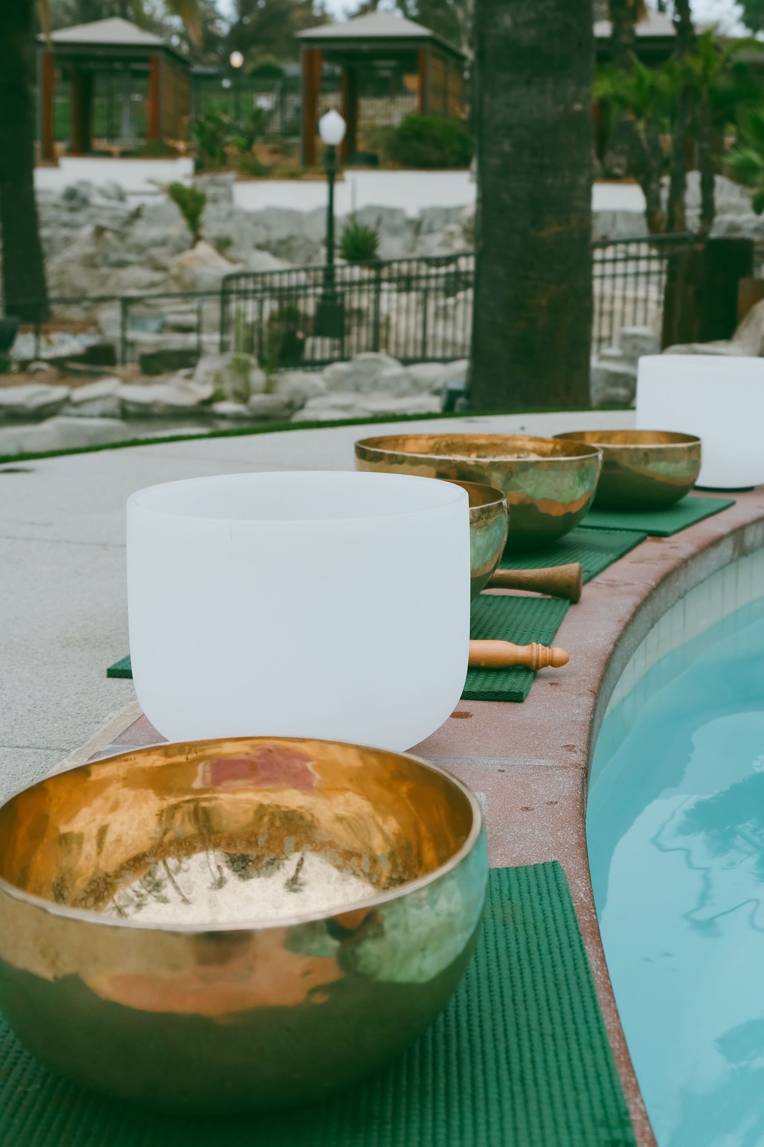 Copper singing bowls and white crystal bowls arranged along pool edge for sound healing ceremony.
