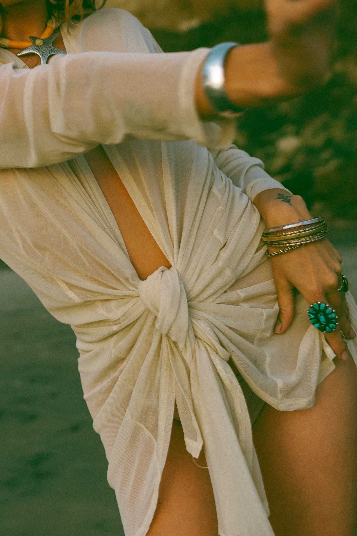Close-up details of a white draped fabric dress with elegant pleating and a turquoise statement ring accessory.