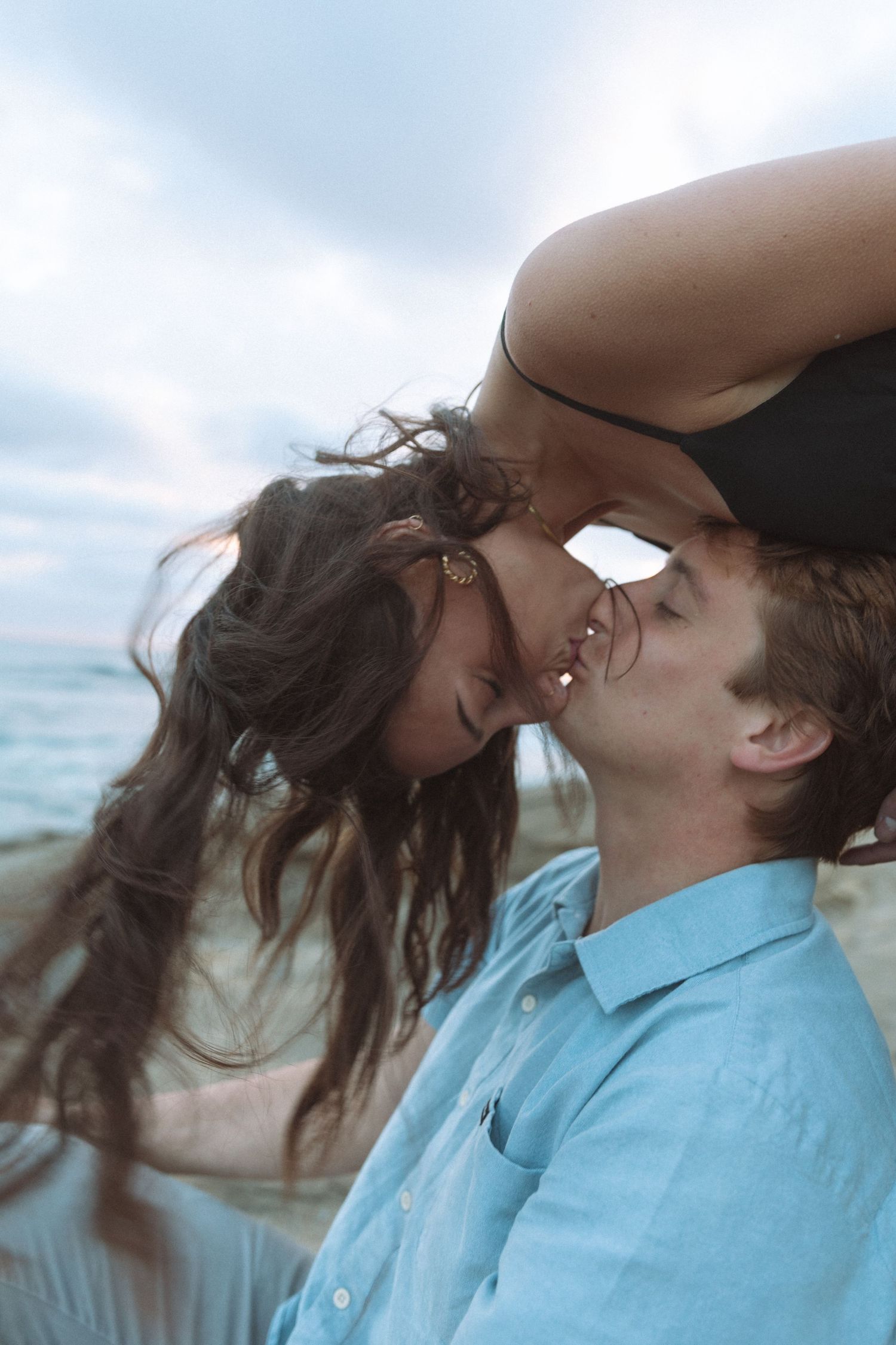Two people share a tender moment against a misty coastal backdrop.