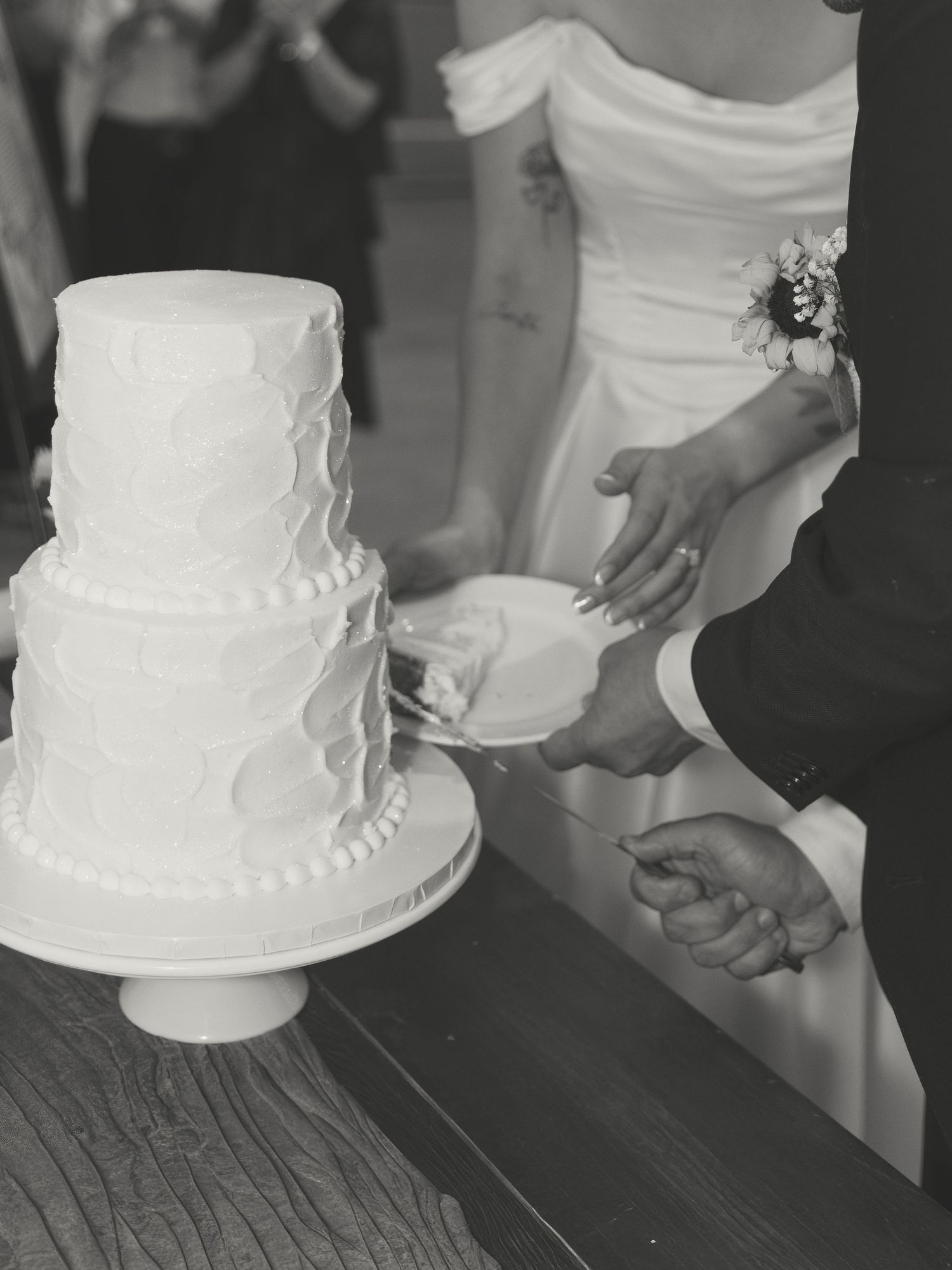 Black and white photo of hands cutting a classic white wedding cake.