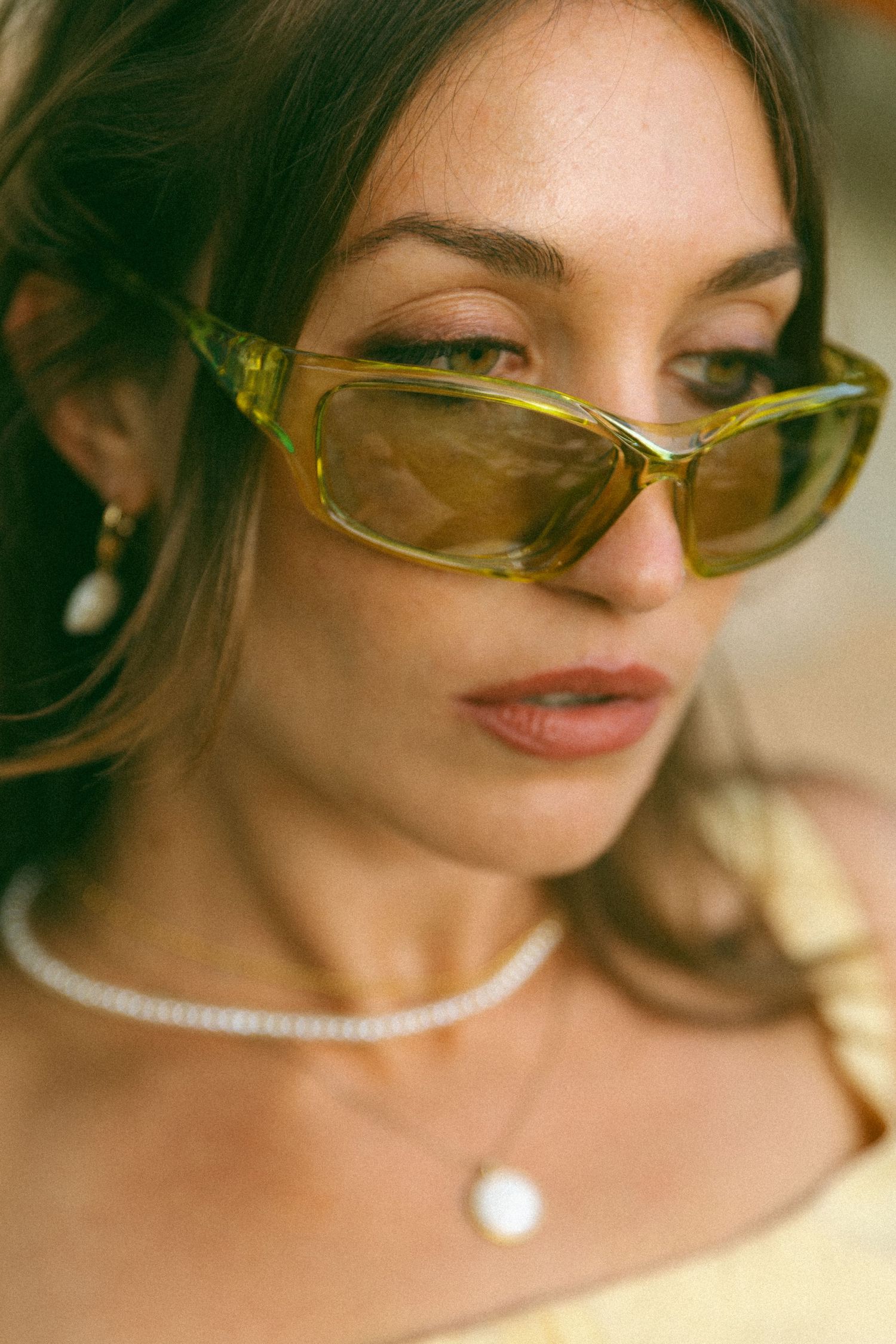 Stylish sunglasses and pearl necklace detail in warm sunlit portrait.