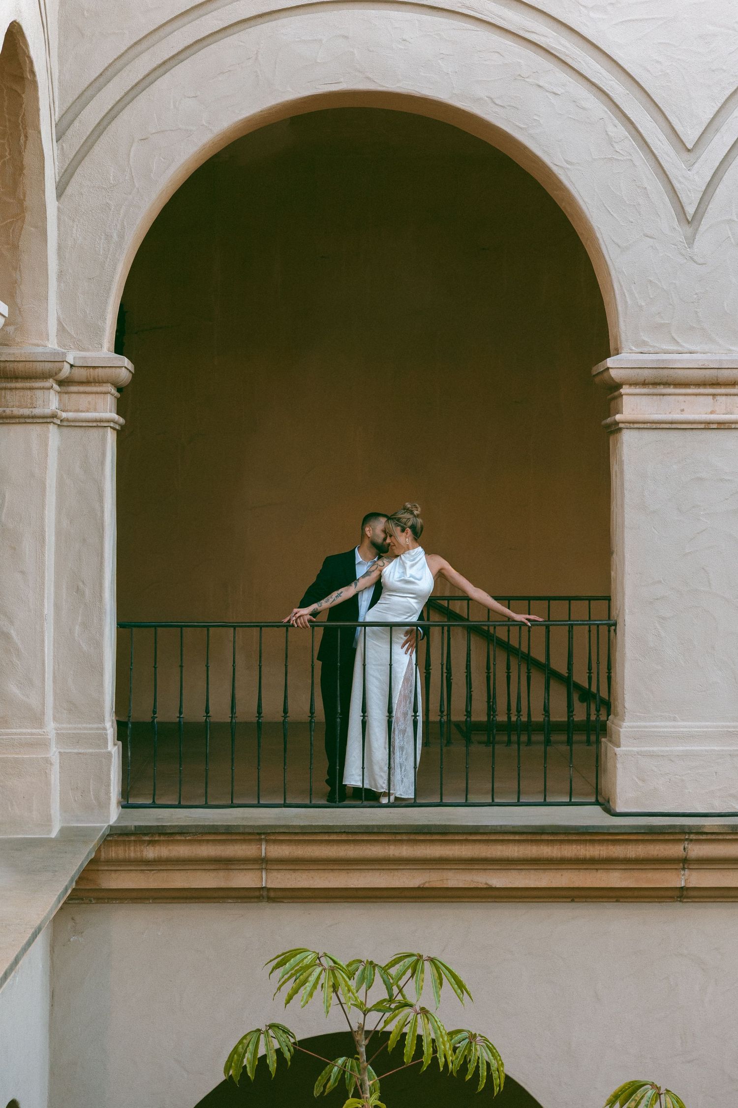 Wedding couple standing together under an elegant archway in formal attire.