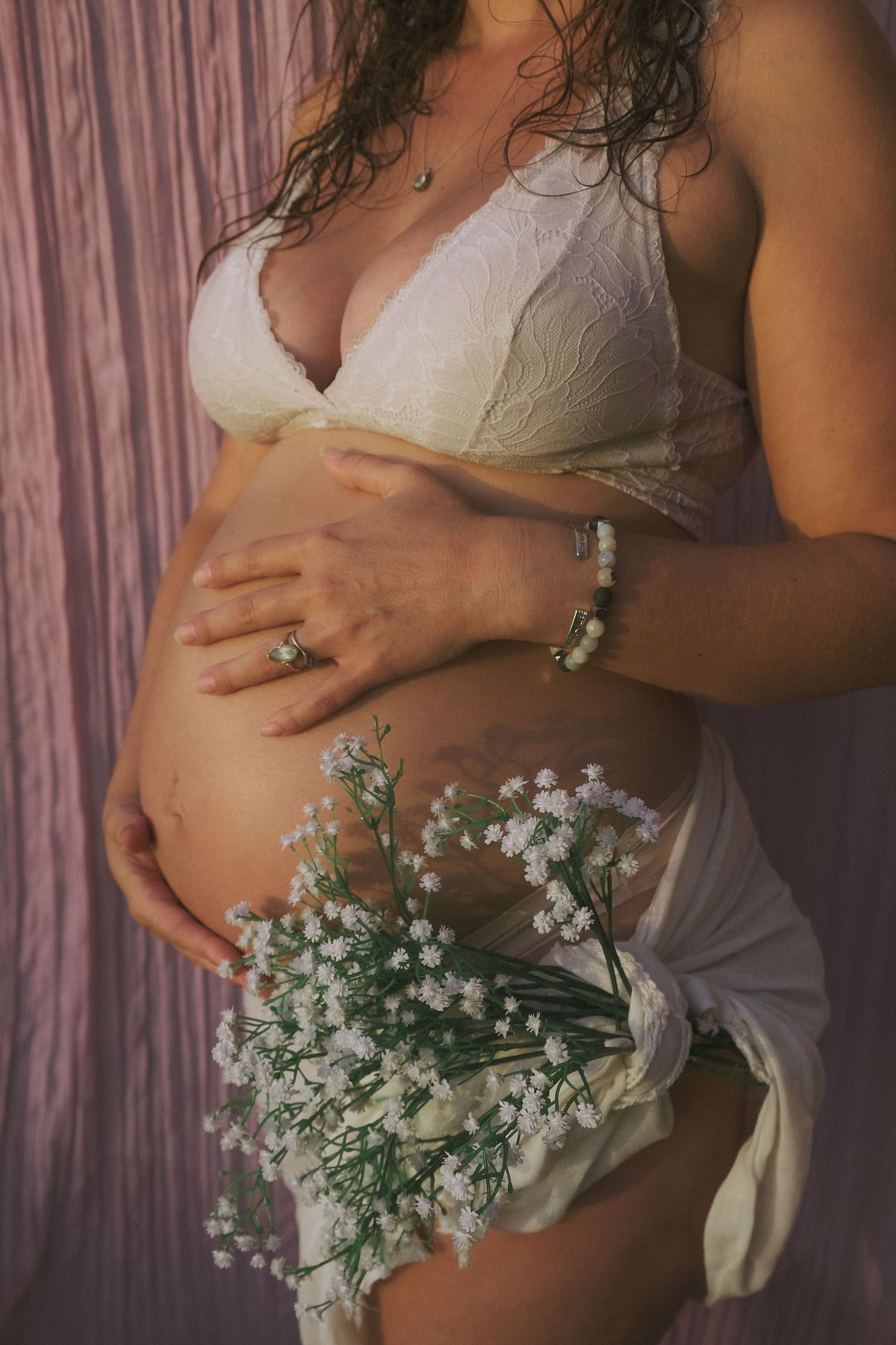 A close-up maternity photo with delicate white baby's breath flowers against a pink backdrop.