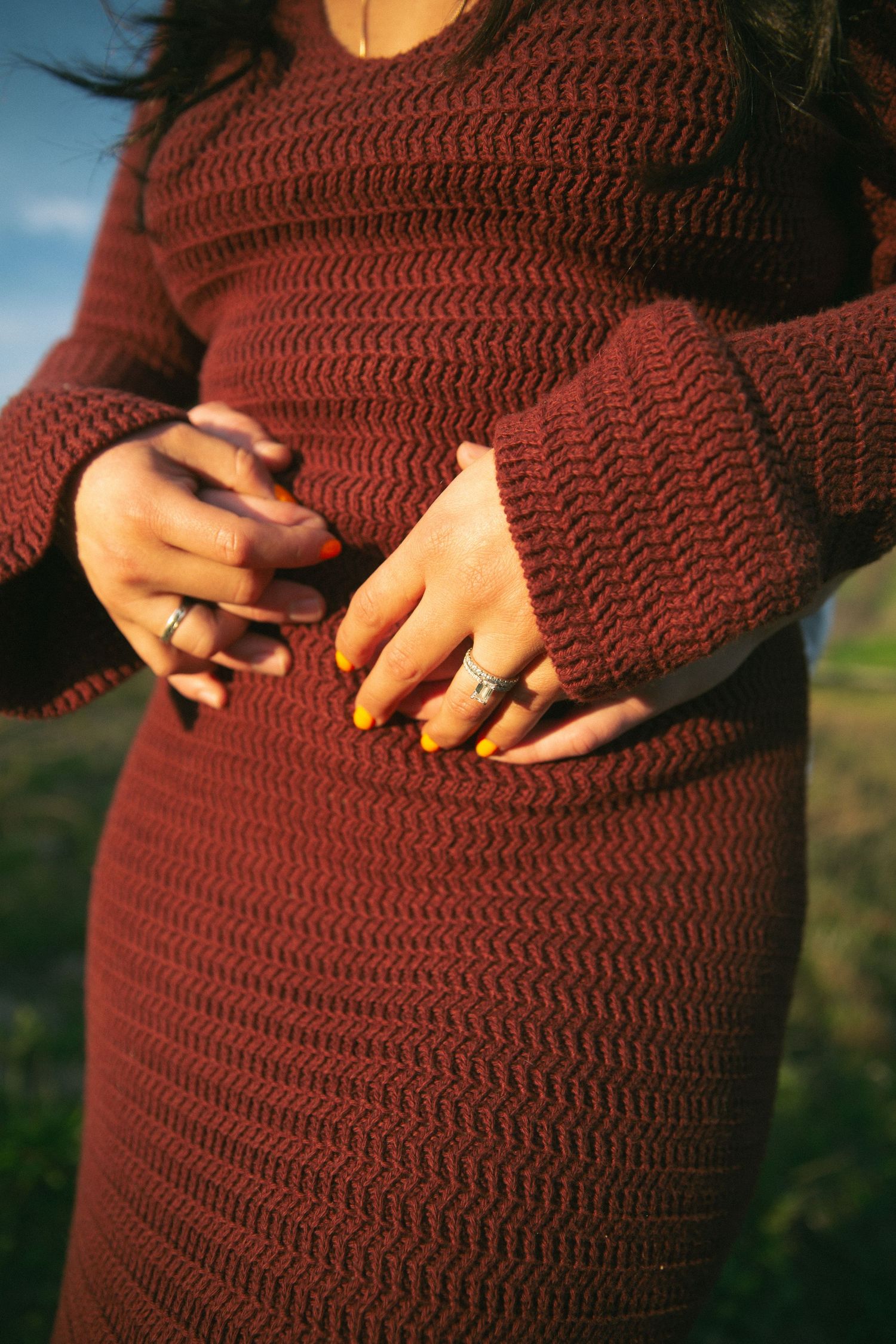 Close-up of hands with rings on a burgundy knit sweater dress.