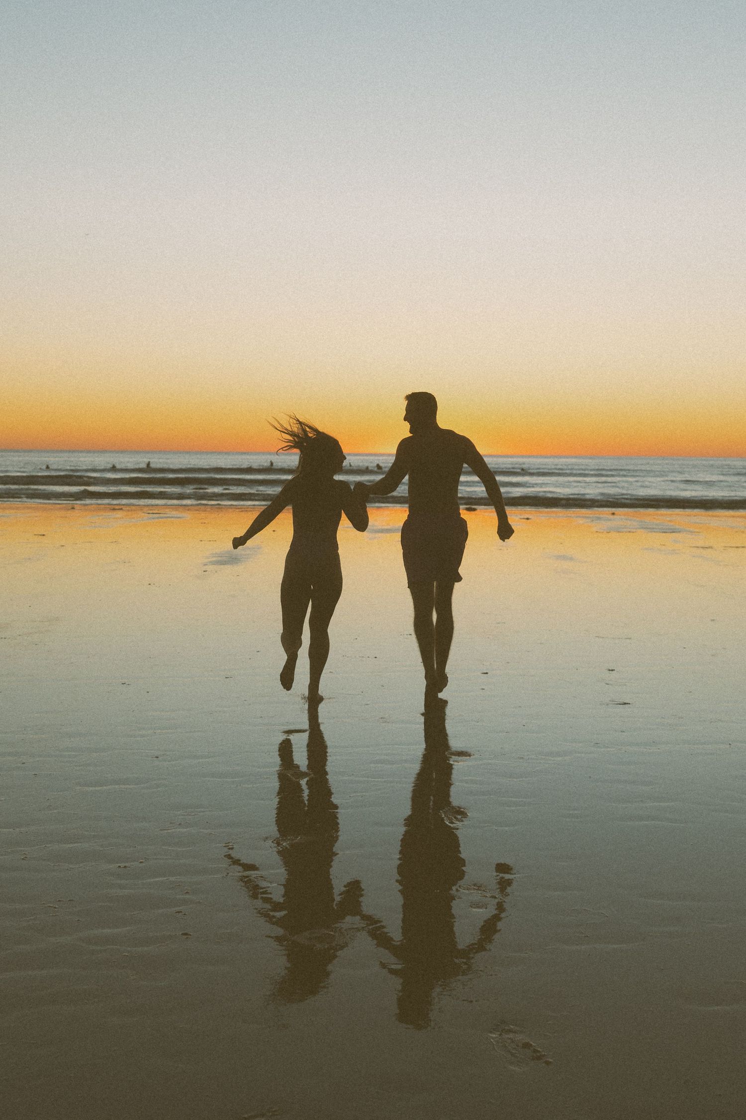 Silhouettes of two people walking and playing on a beach at sunset.