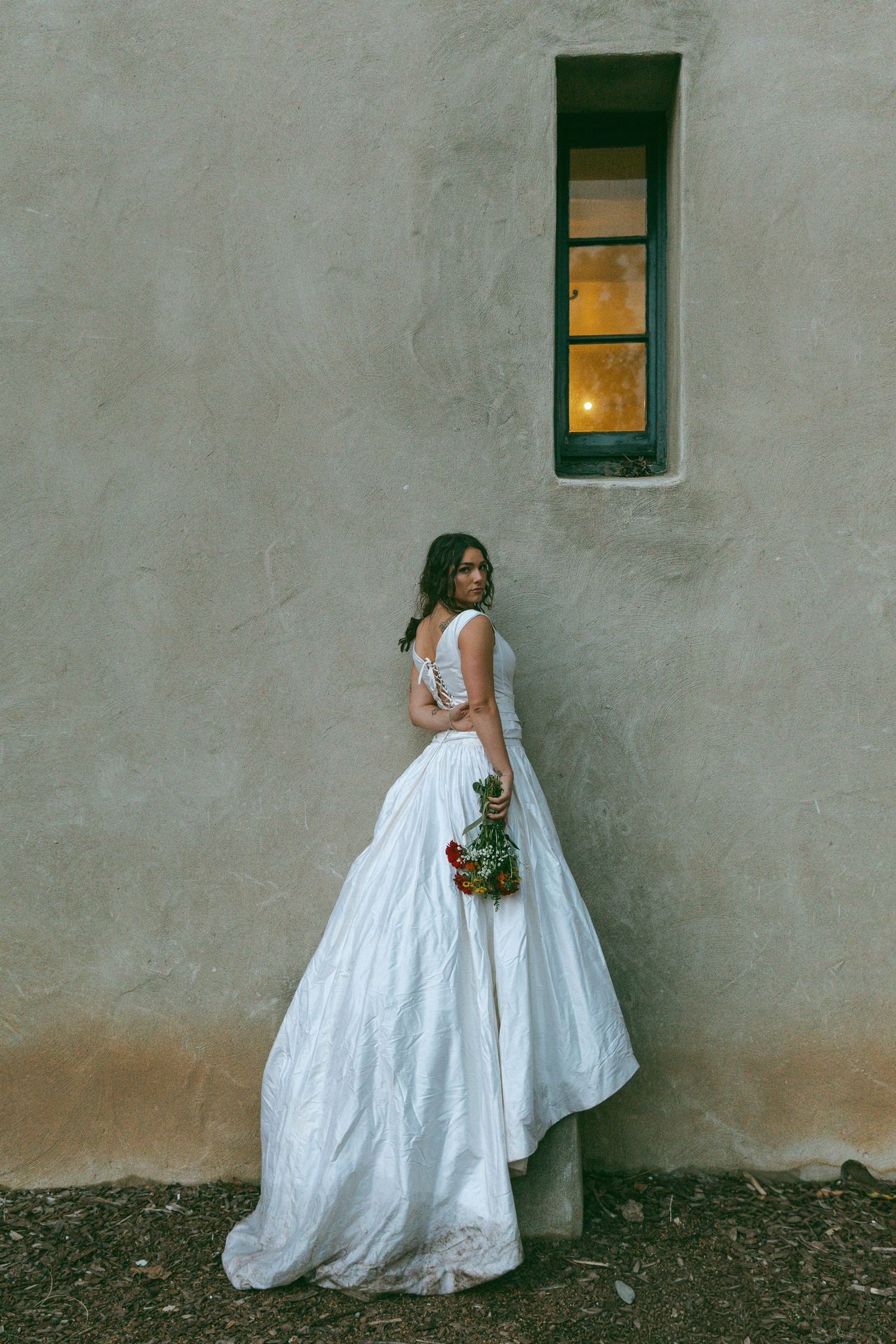 A white wedding dress photographed against a minimalist gray wall with a small window.