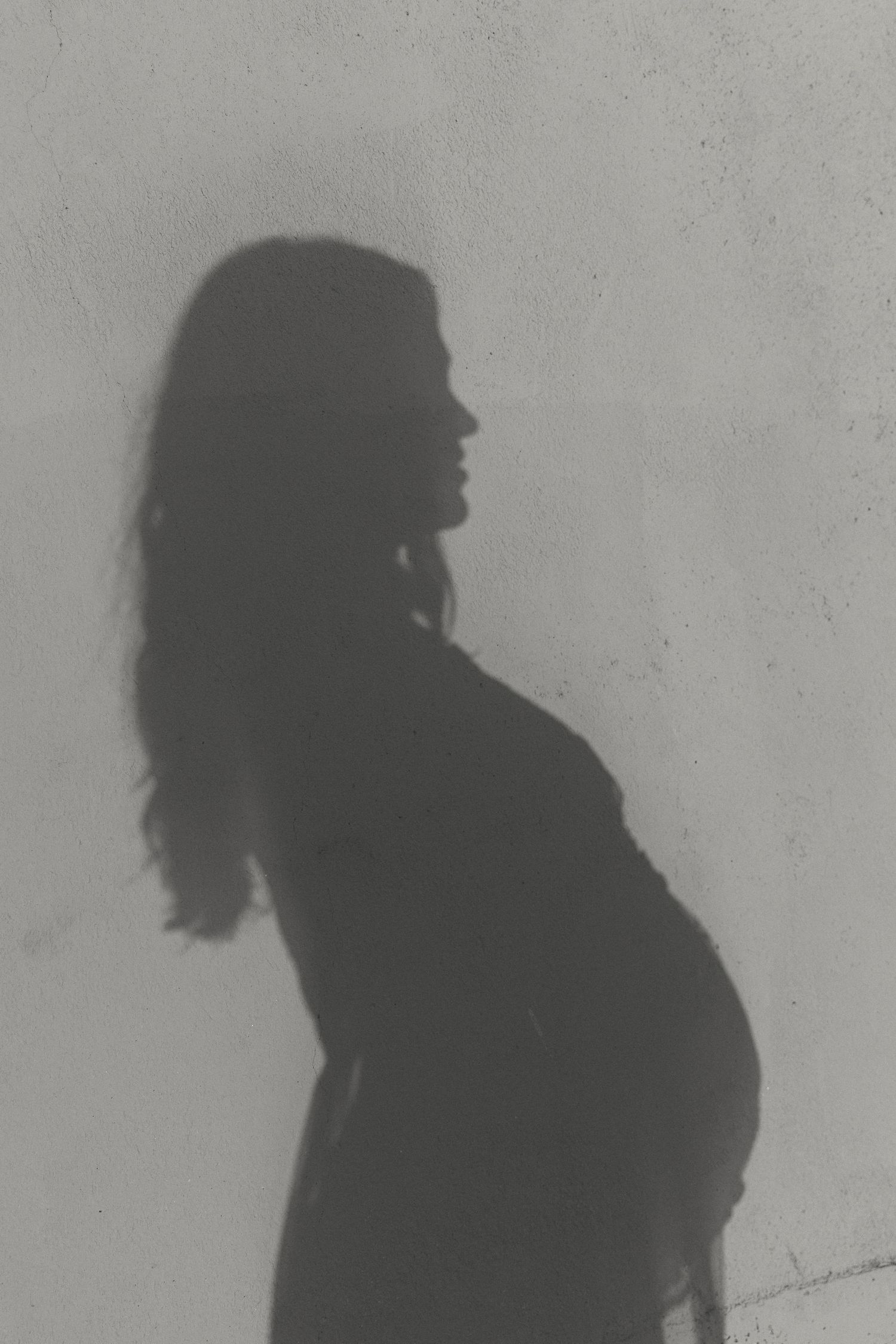 Artistic silhouette profile of pregnant figure against light wall.