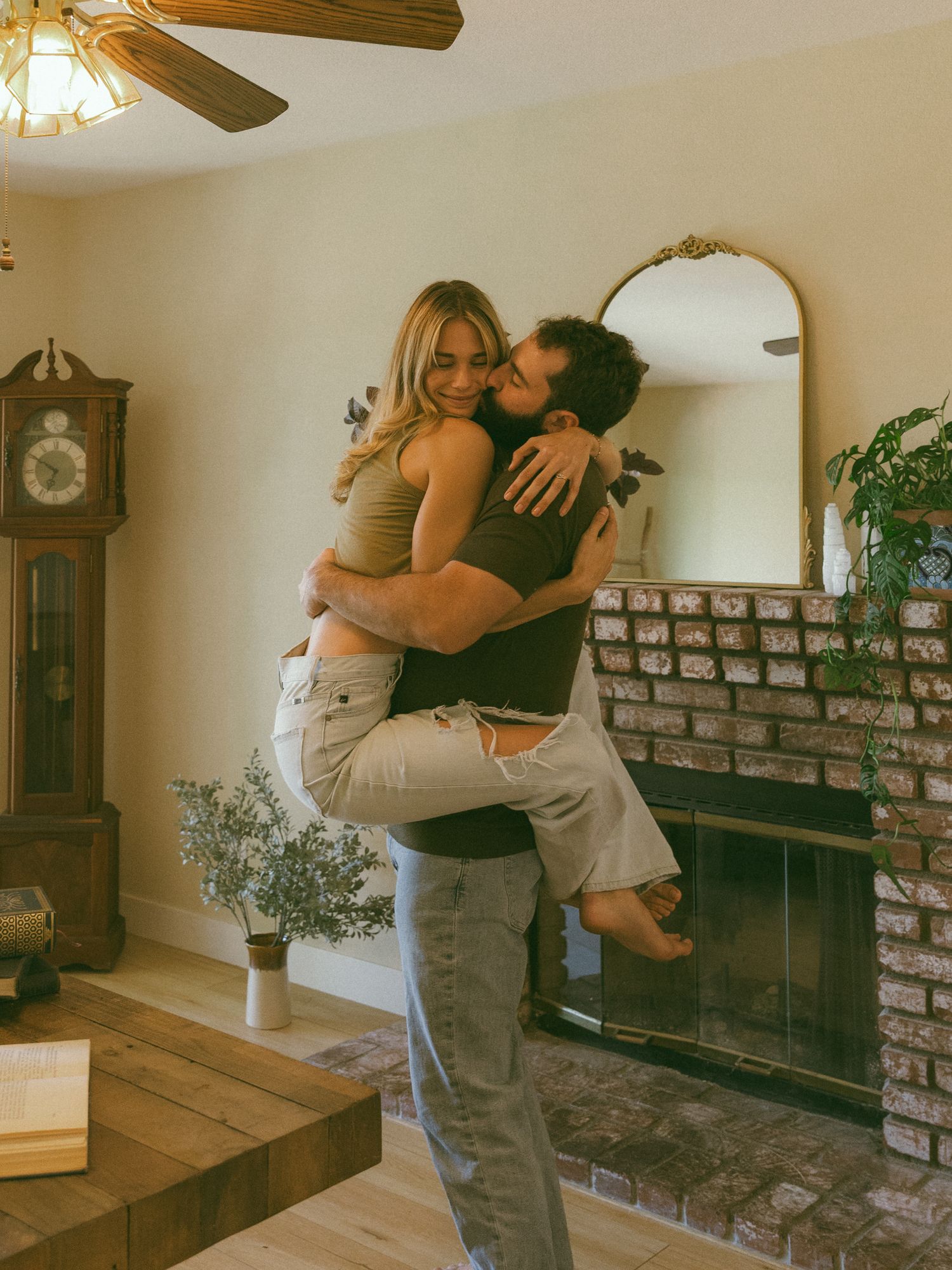 A series of romantic embrace photos taken in front of a rustic brick wall with a grandfather clock.
