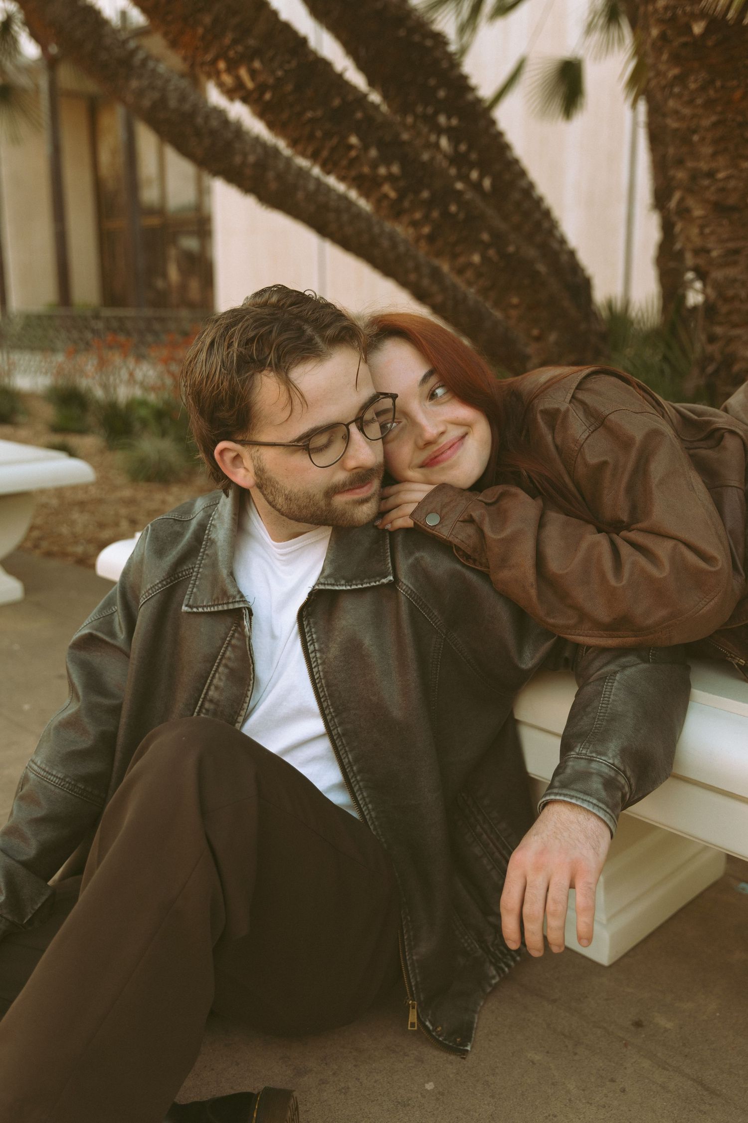 Intimate couple relaxing on wooden bench under tree branches.
