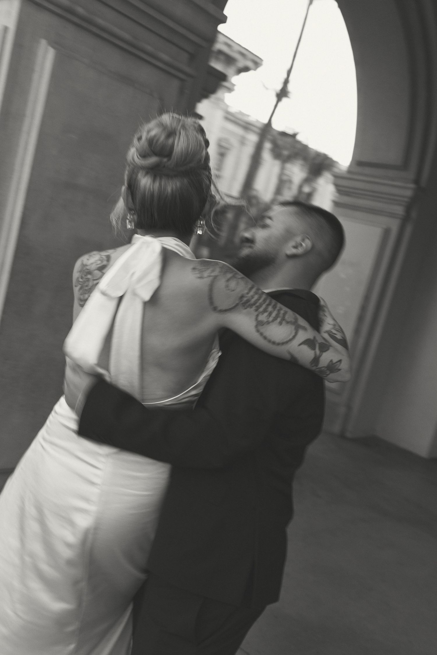 Artistic black and white photo of a couple dancing in formal attire under an archway.