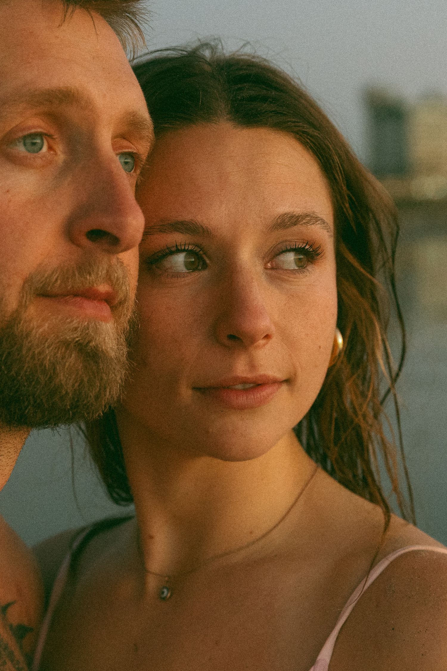 Close-up portrait of a couple at golden hour with soft lighting and urban backdrop.