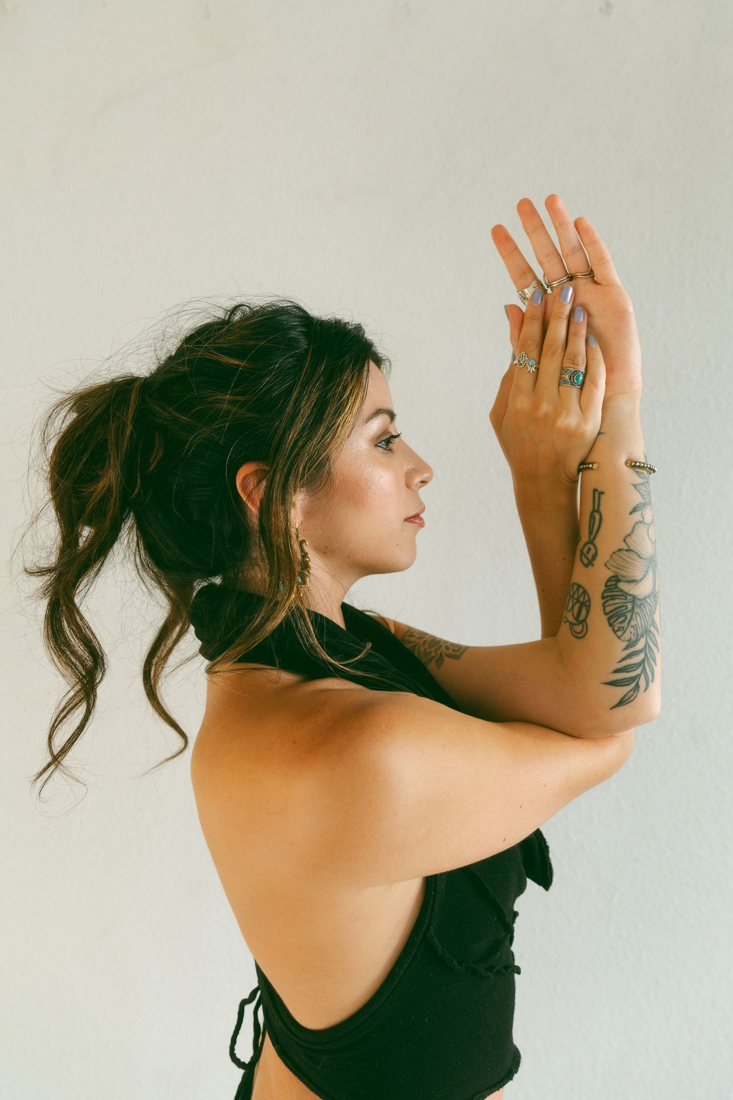 Artistic portrait showing tattoos and rings with arms raised against white background.