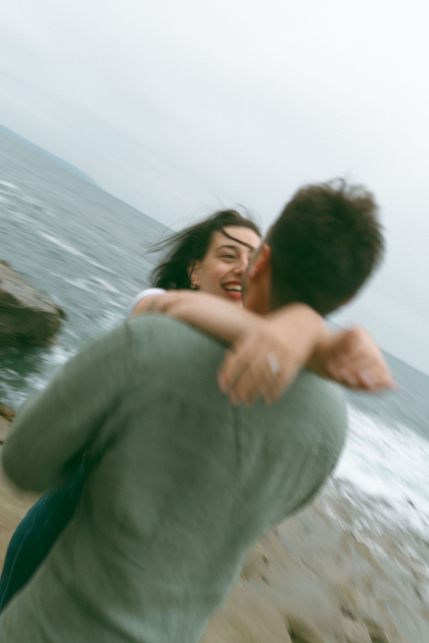 A blurred action shot of a couple spinning and embracing by the ocean.