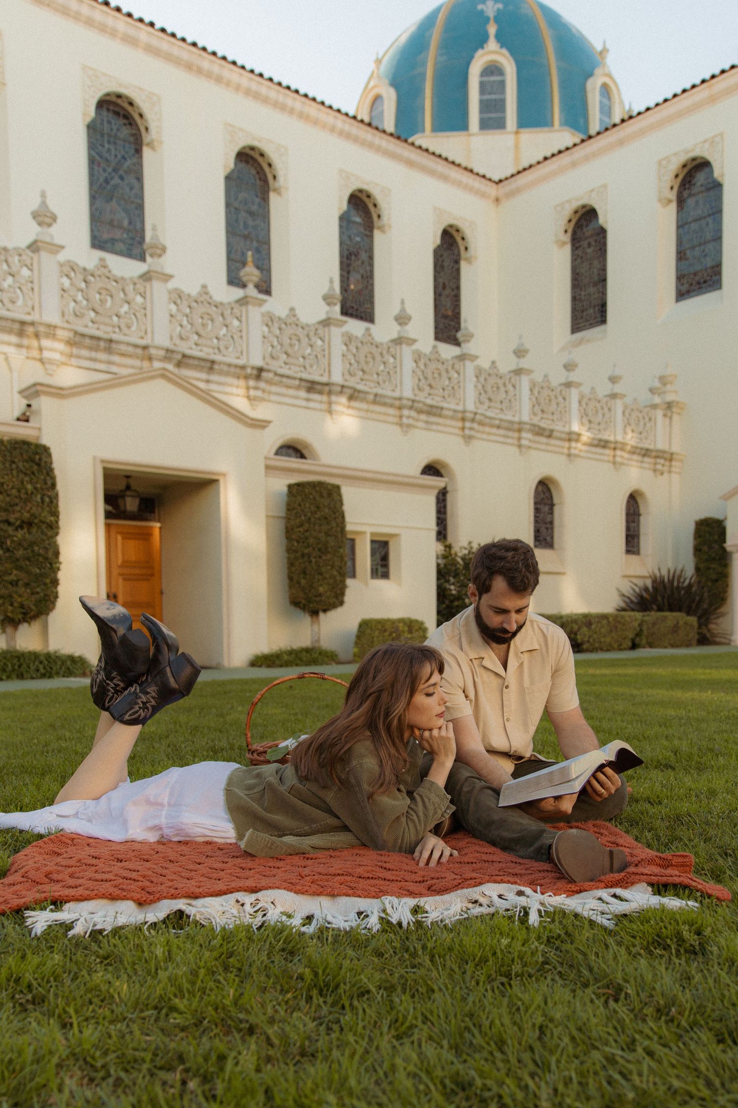 A couple reads together on a blanket outside a beautiful Spanish colonial church.