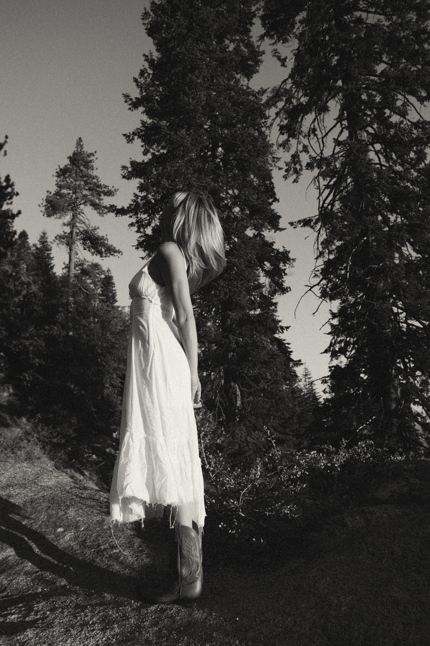 Artistic black and white photo of someone in a white dress standing in a forest.