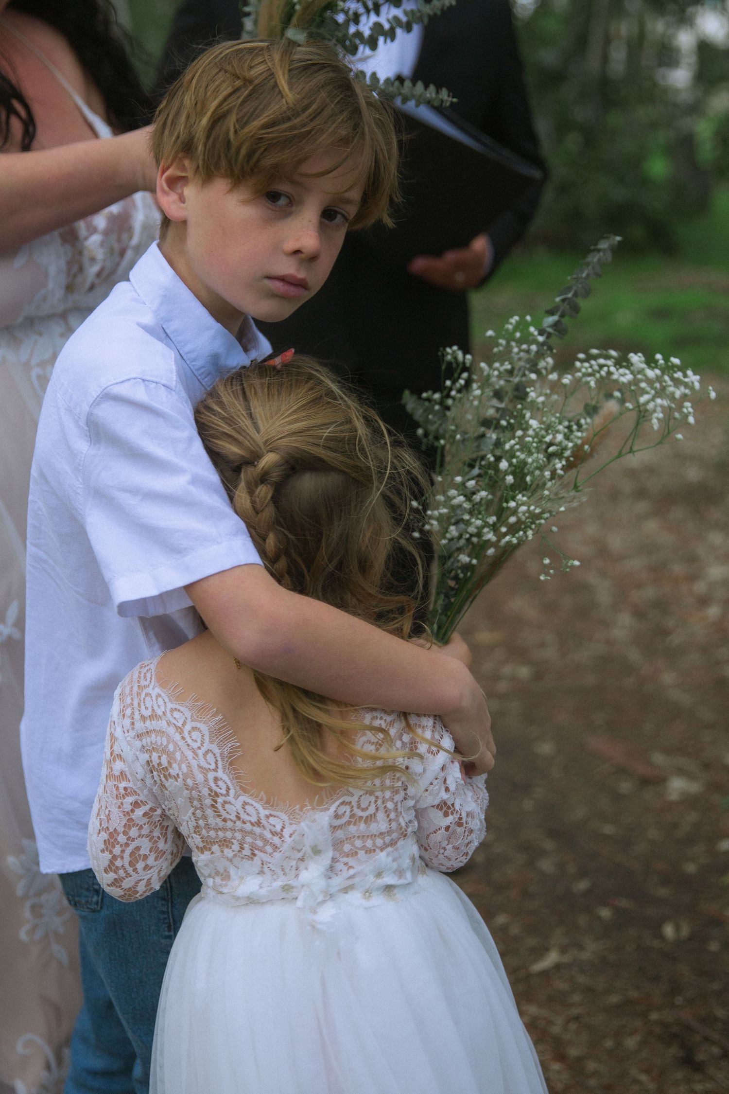 Young attendants in white attire holding delicate baby's breath flowers at an outdoor ceremony.