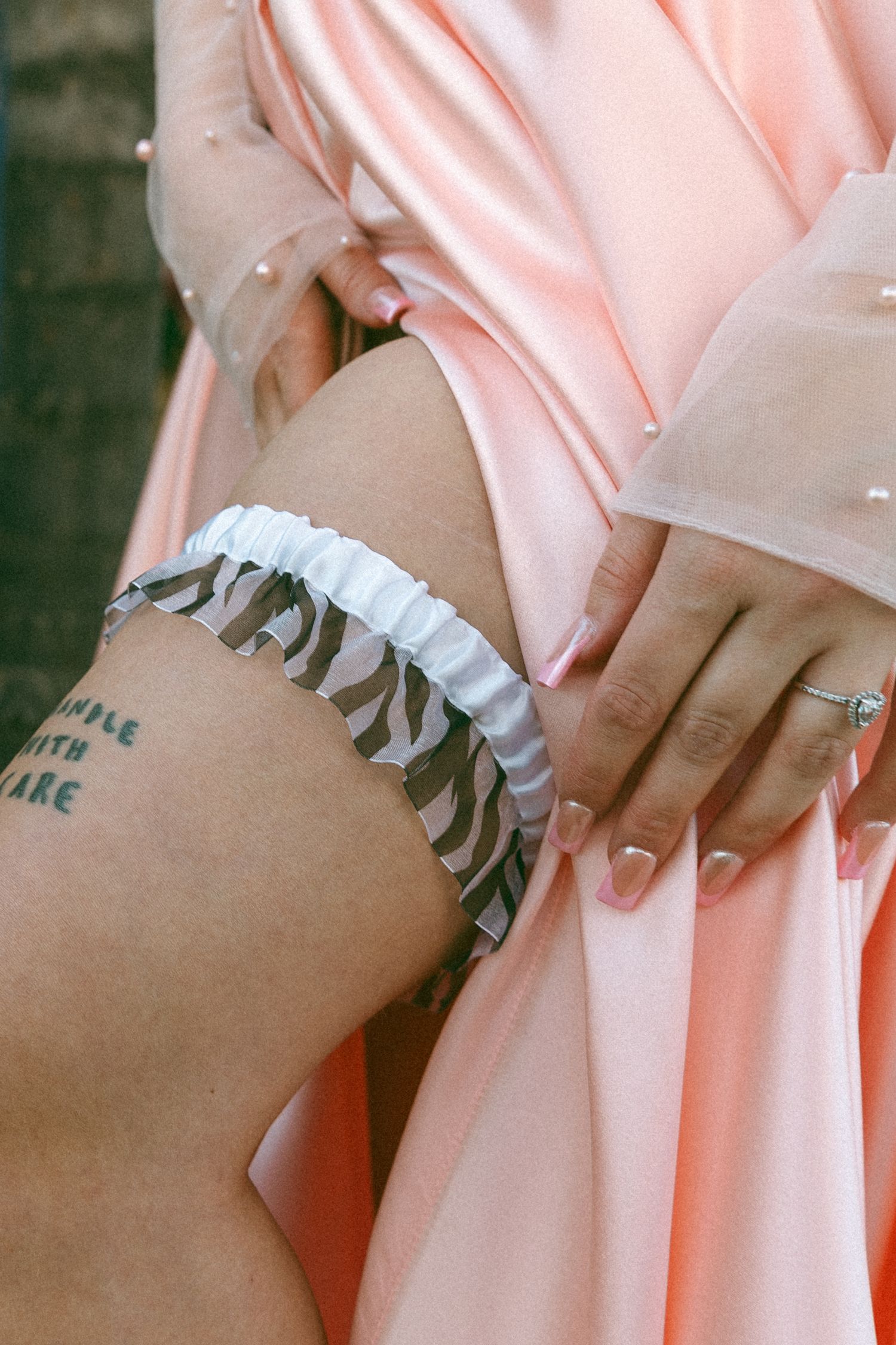 Detail shot of white garter on leg with pink dress fabric.