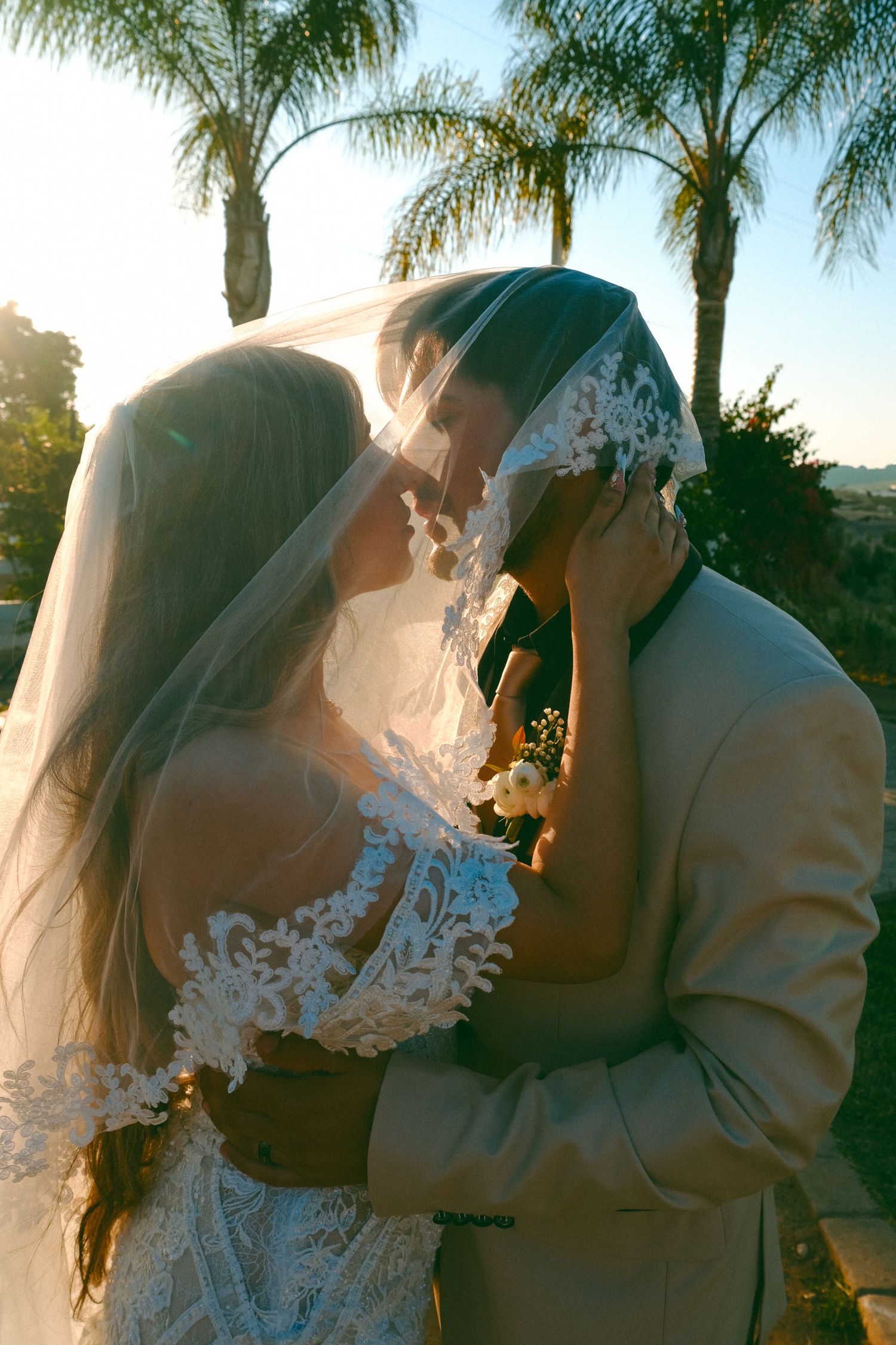 Romantic sunset wedding photo showing a couple in an intimate moment with palm trees in the background.