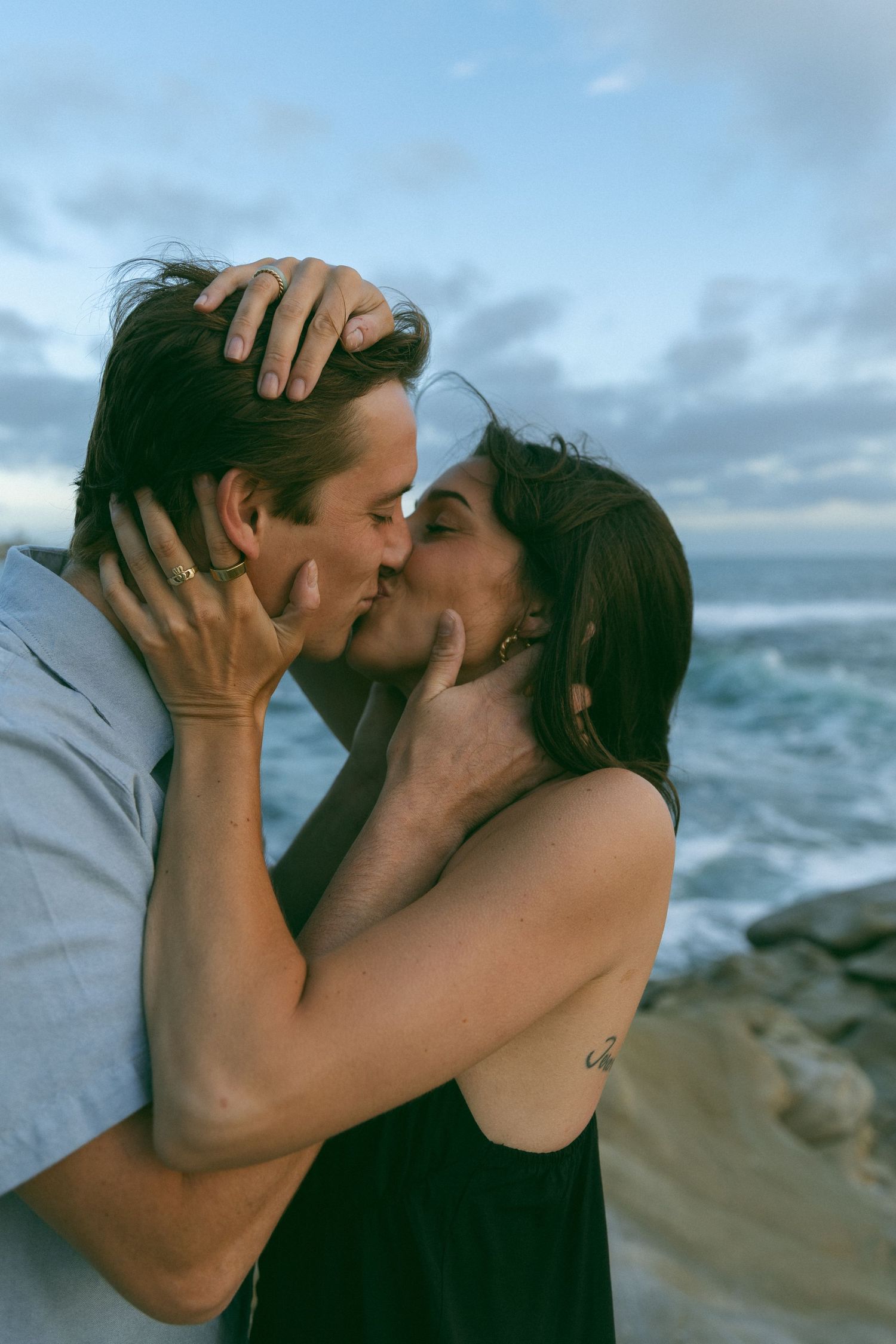 Romantic embrace against ocean backdrop with dramatic cloudy sky.