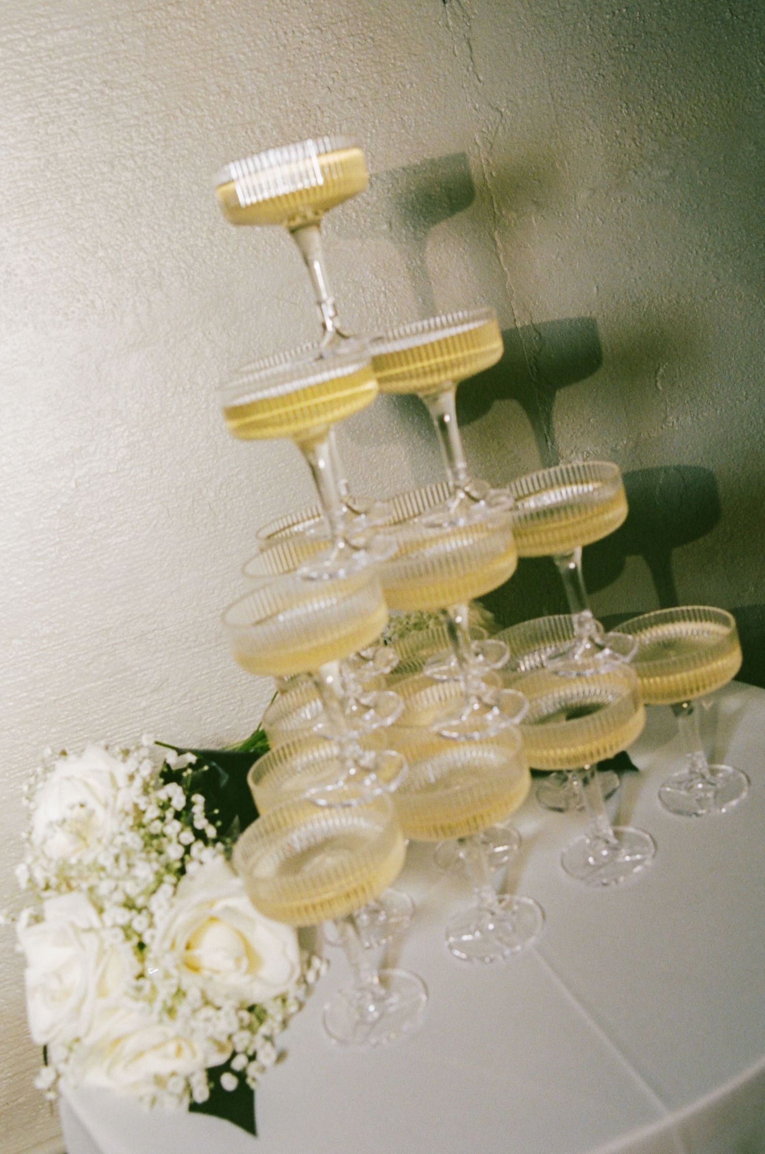 Elegant champagne tower with coupe glasses and white roses at wedding reception.