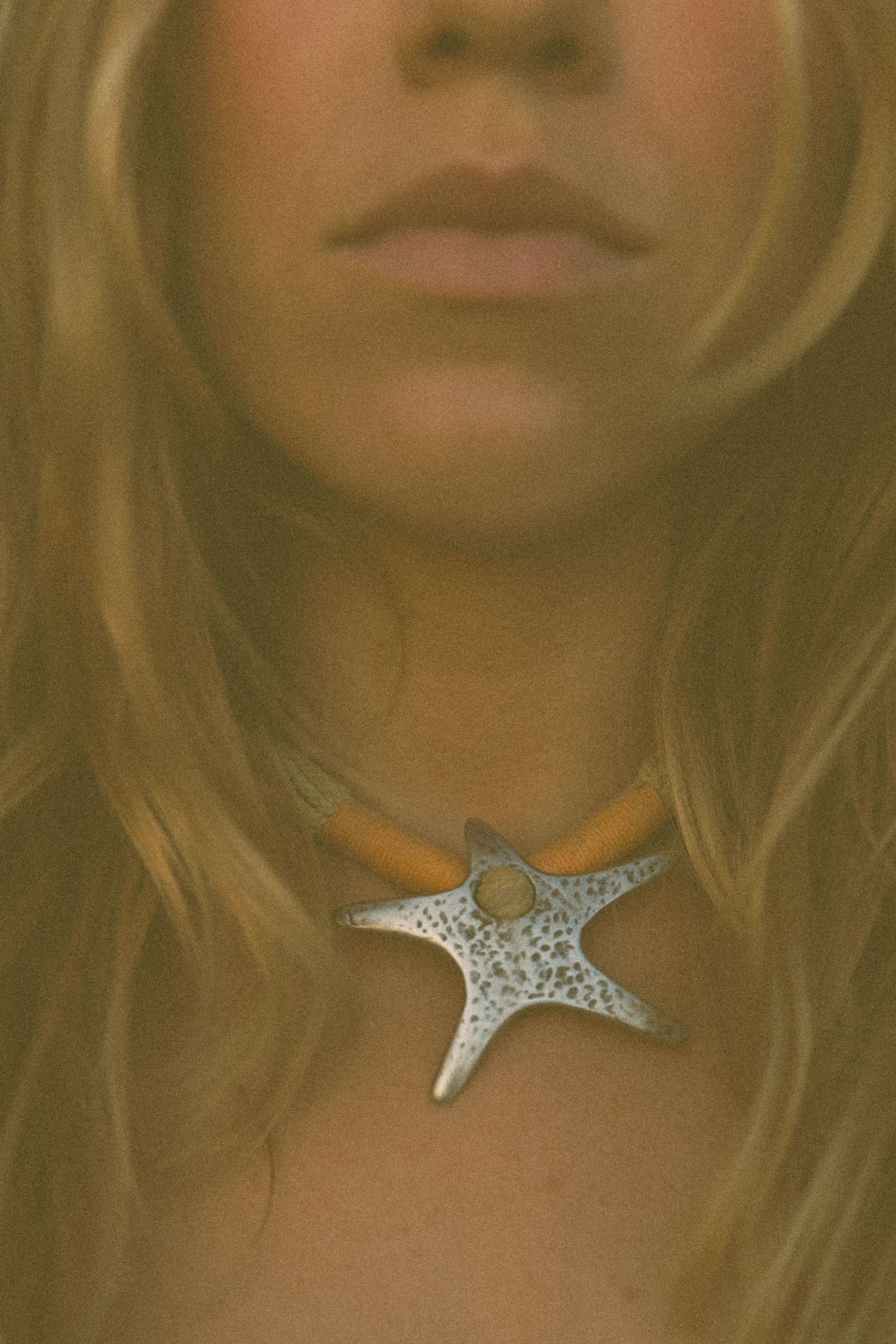 A decorative silver starfish pendant necklace worn against a soft-focus background with blonde hair.