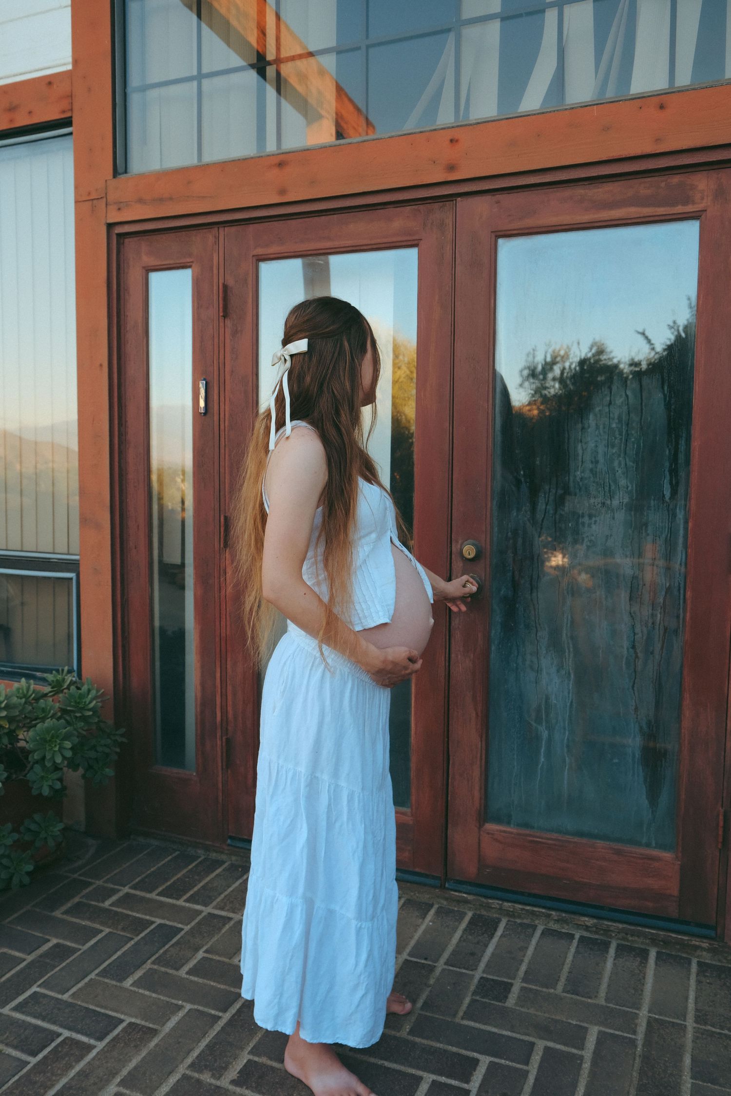 A side view of an expectant mother in white standing by wooden doors.