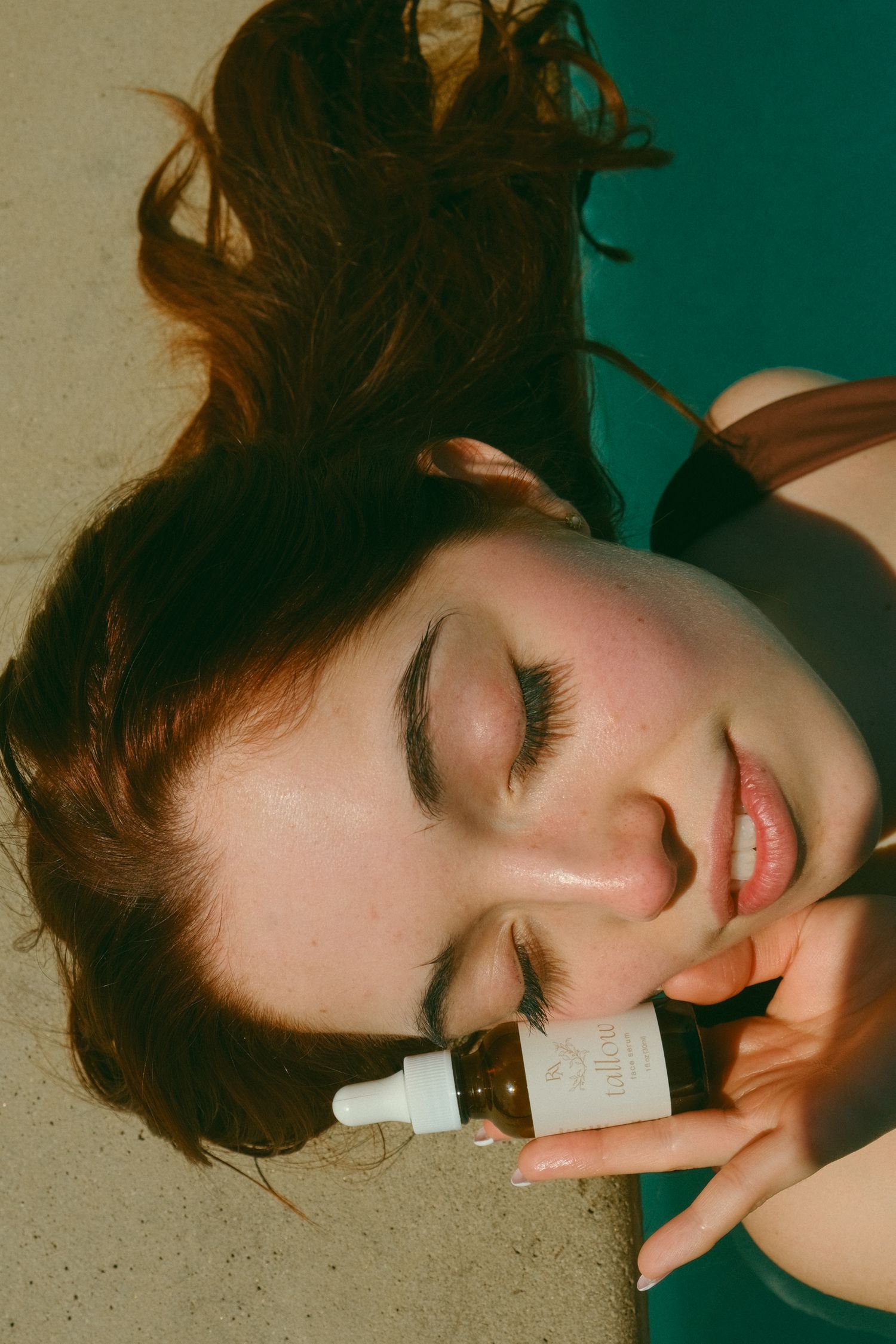 Artistic beauty product photo showing relaxed pose with bottles against teal background.