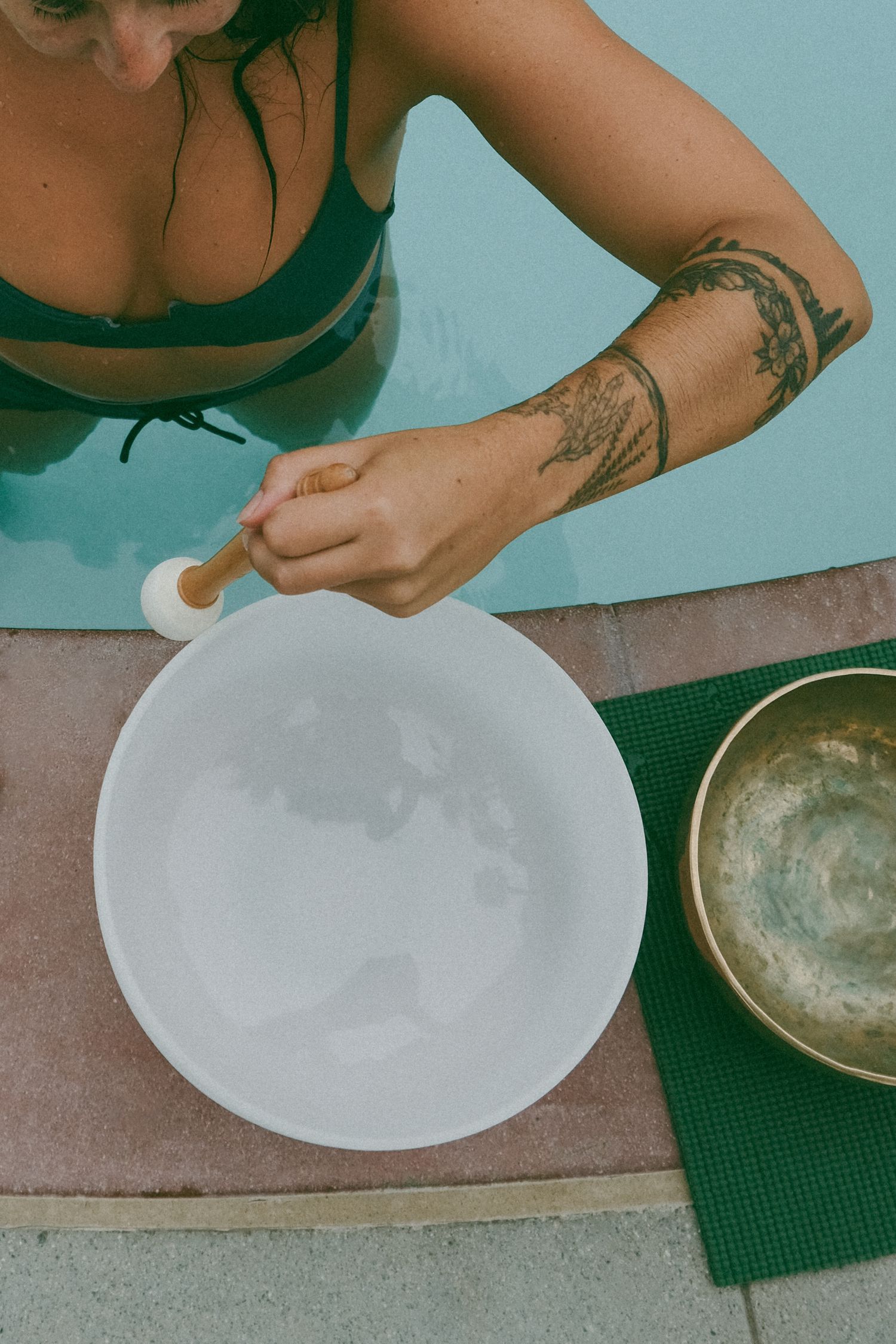 Close-up of tattooed arm preparing white crystal bowl for sound healing ceremony.