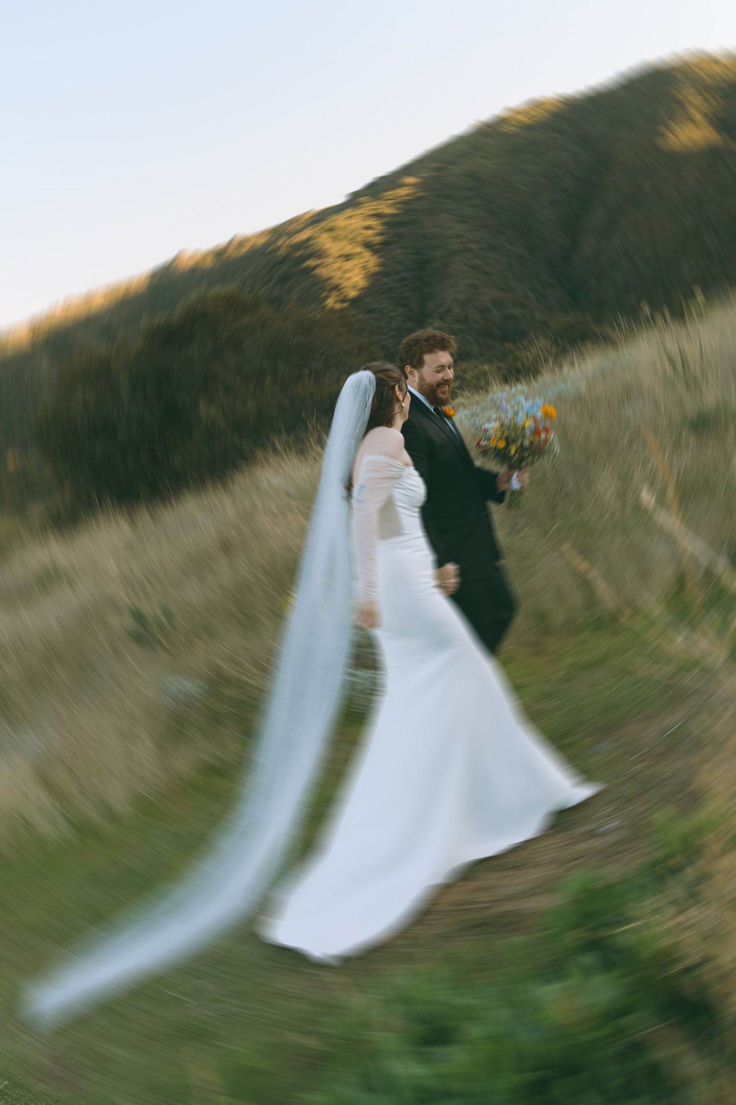 Motion-blurred wedding photo capturing movement against hillside backdrop.