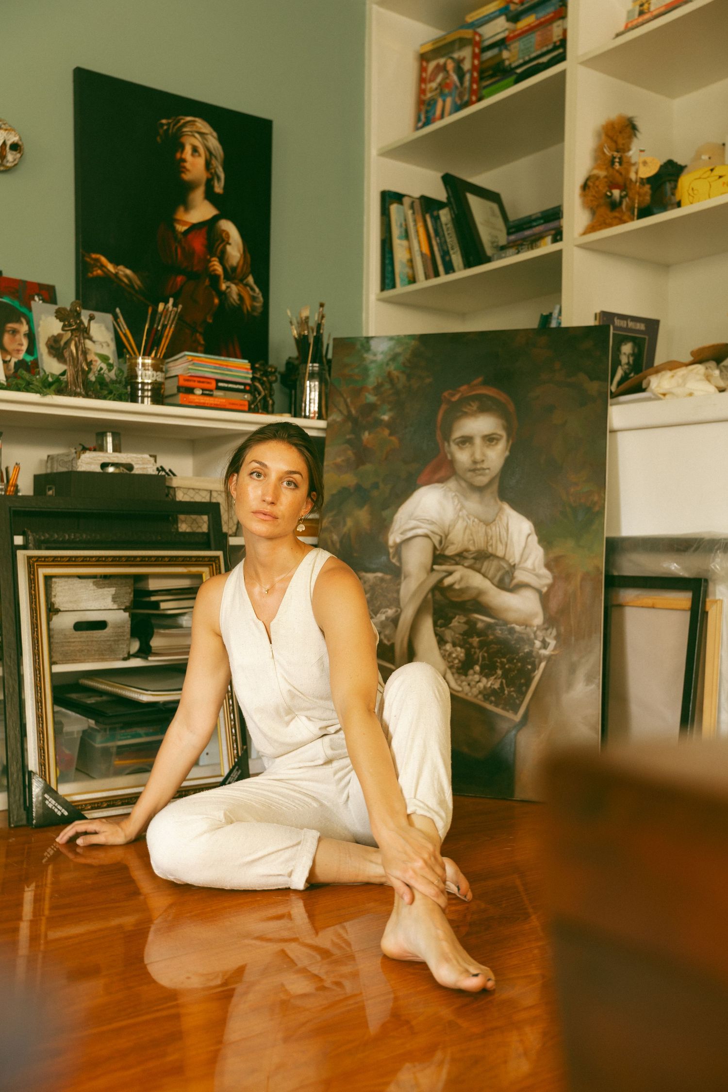 Figure in white clothing creates artistic poses on hardwood floor with bookshelves in background.