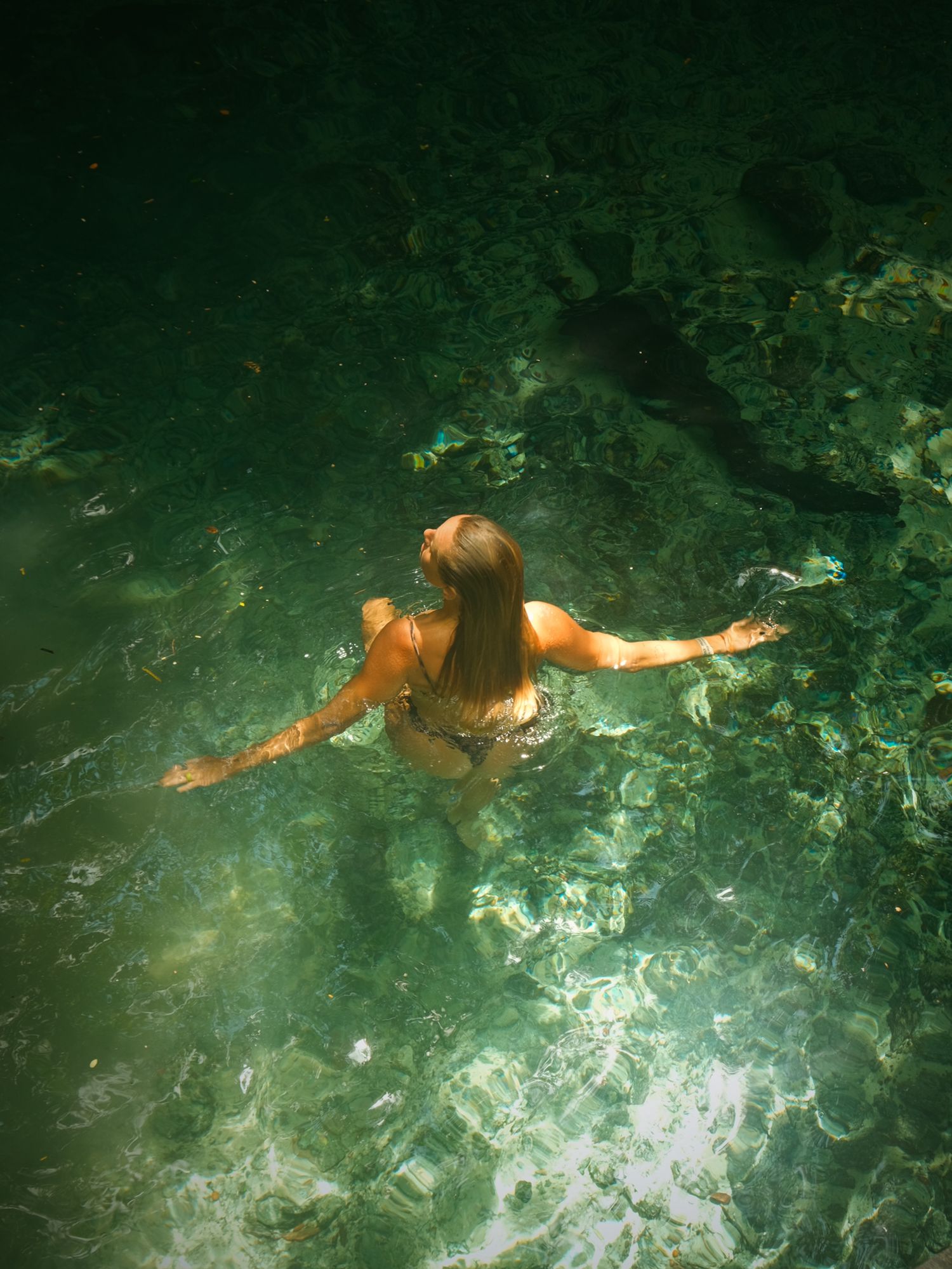 A swimmer floats peacefully in crystal clear turquoise waters surrounded by natural rock formations.