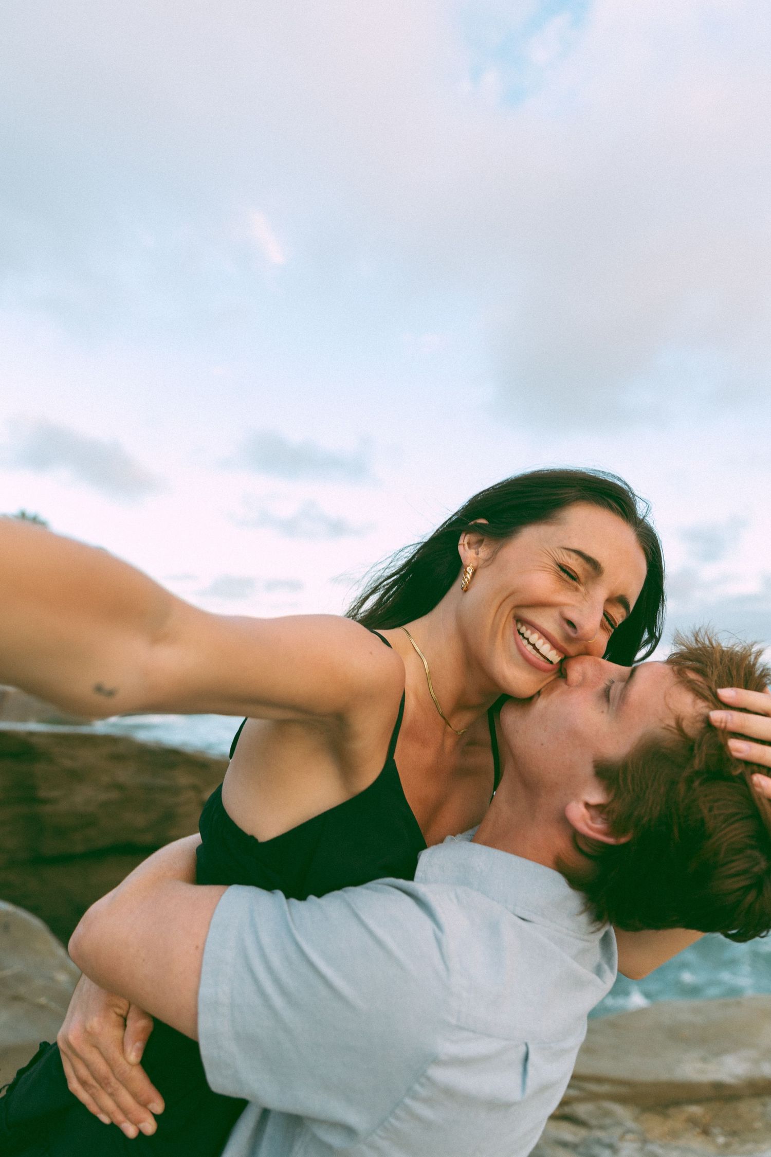 Two people share an intimate moment while laughing together near the sea.