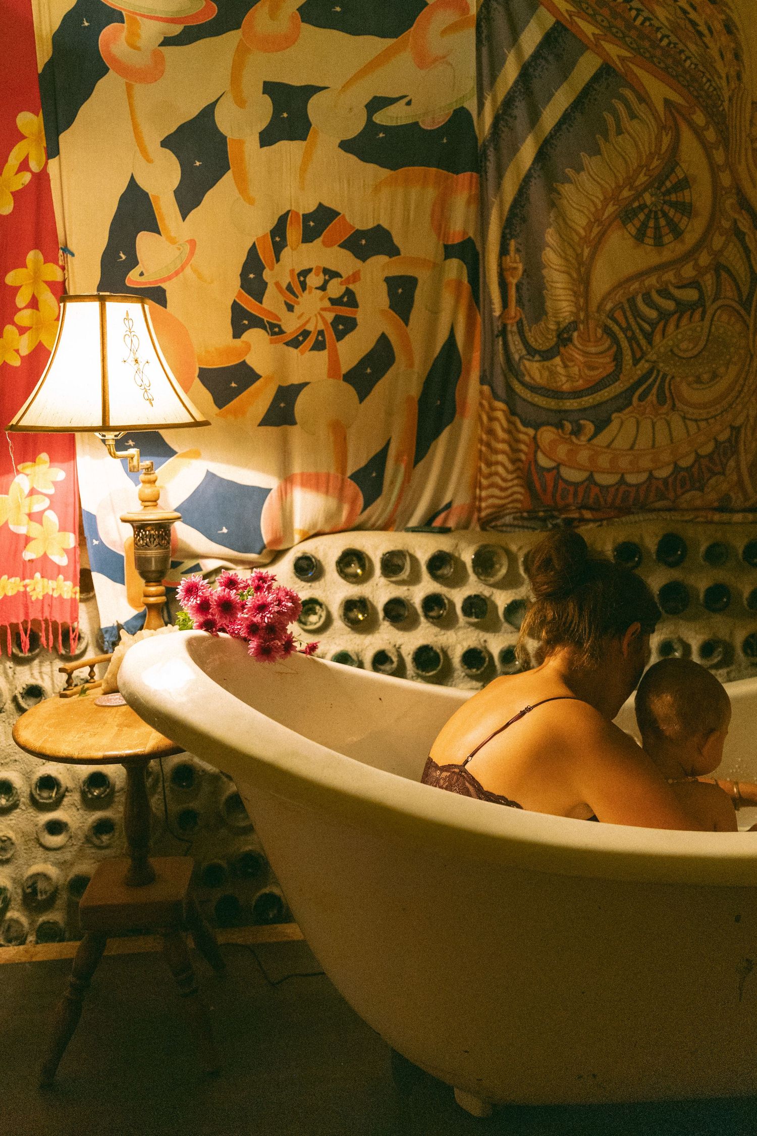 Bathtub scene with decorative wall tapestries and warm lamp lighting creating cozy atmosphere.