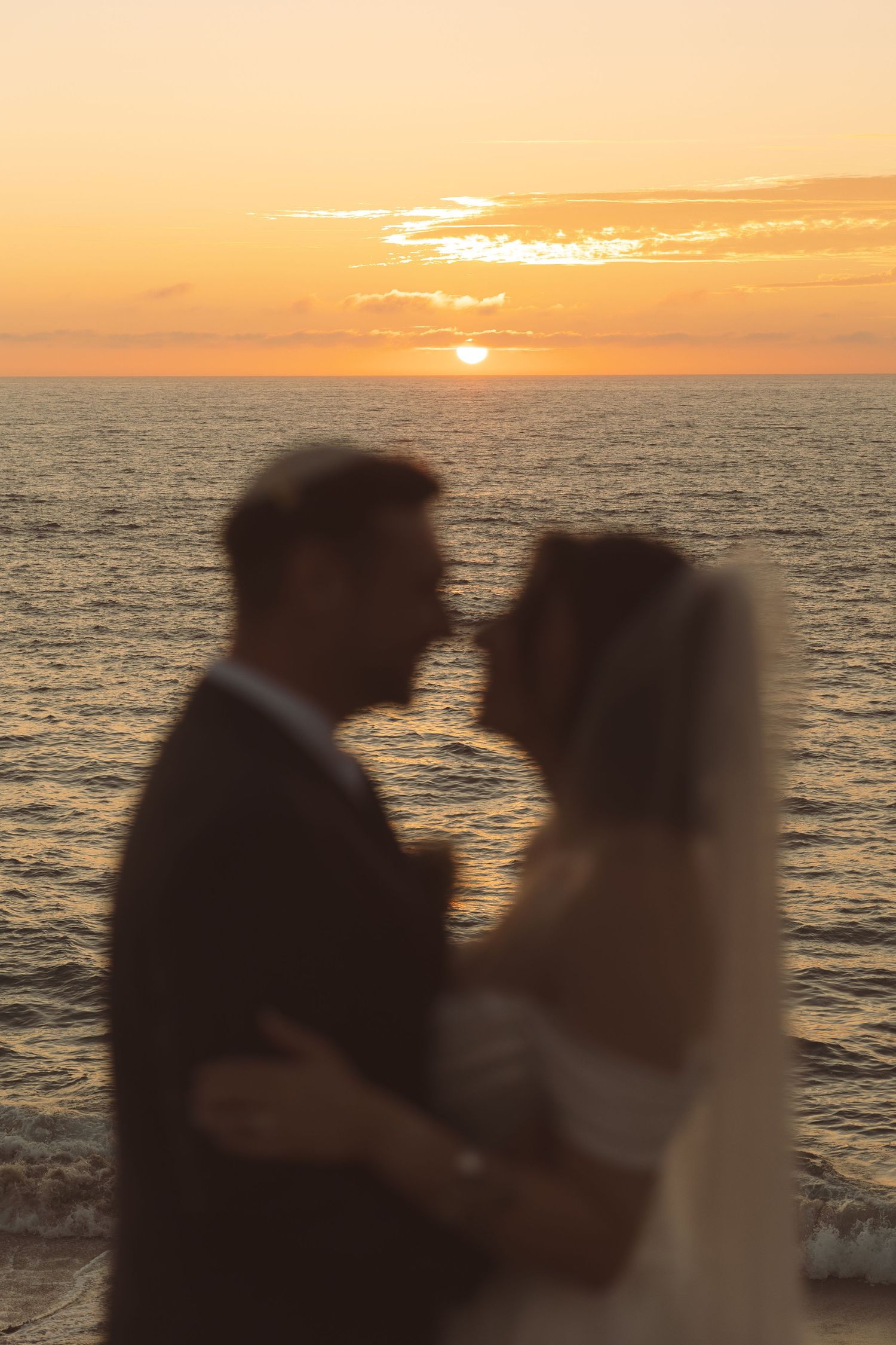 Silhouettes of a couple against a vibrant orange sunset over the ocean.