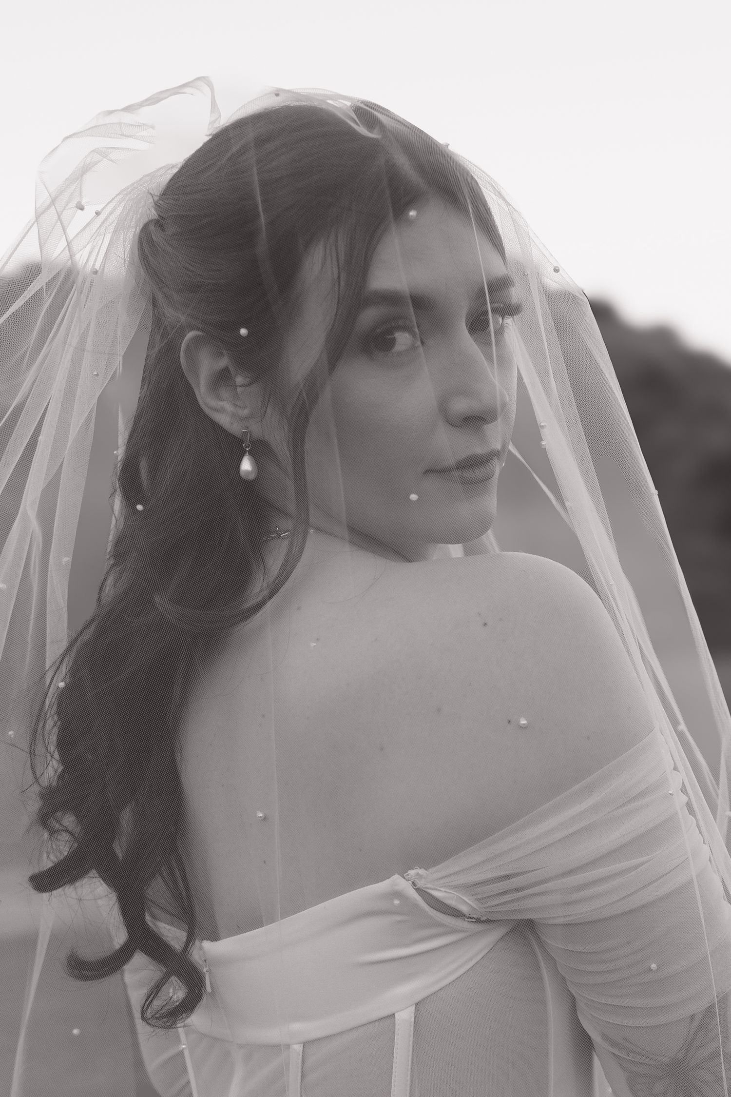 Artistic black and white bridal portrait featuring an off-shoulder dress and flowing veil.