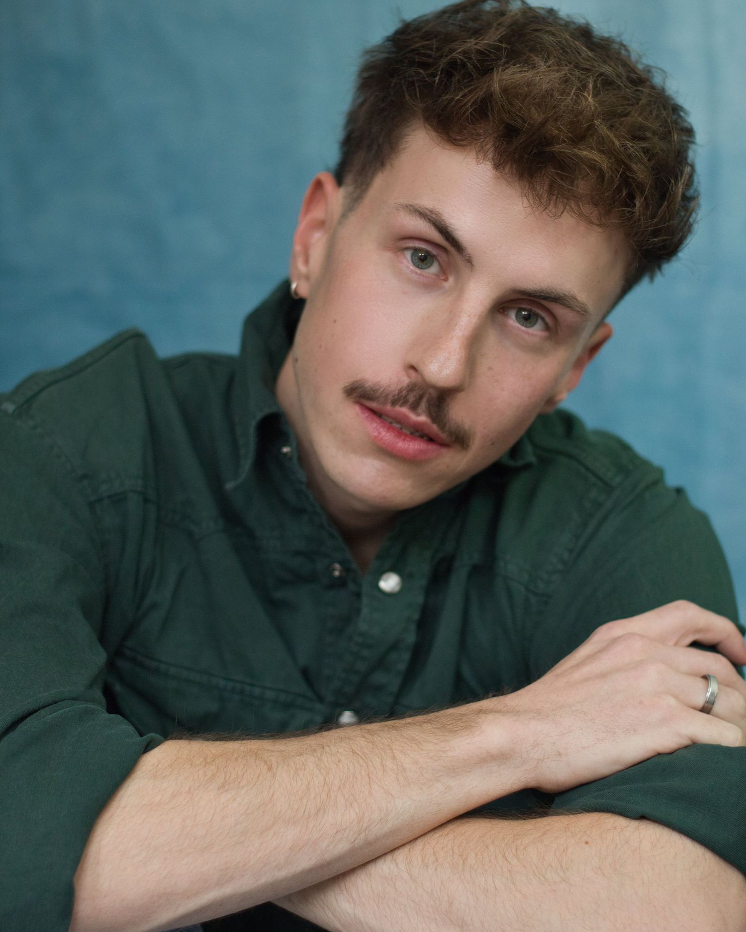 Portrait series of someone wearing a dark green button-up shirt against a blue background in various relaxed poses.