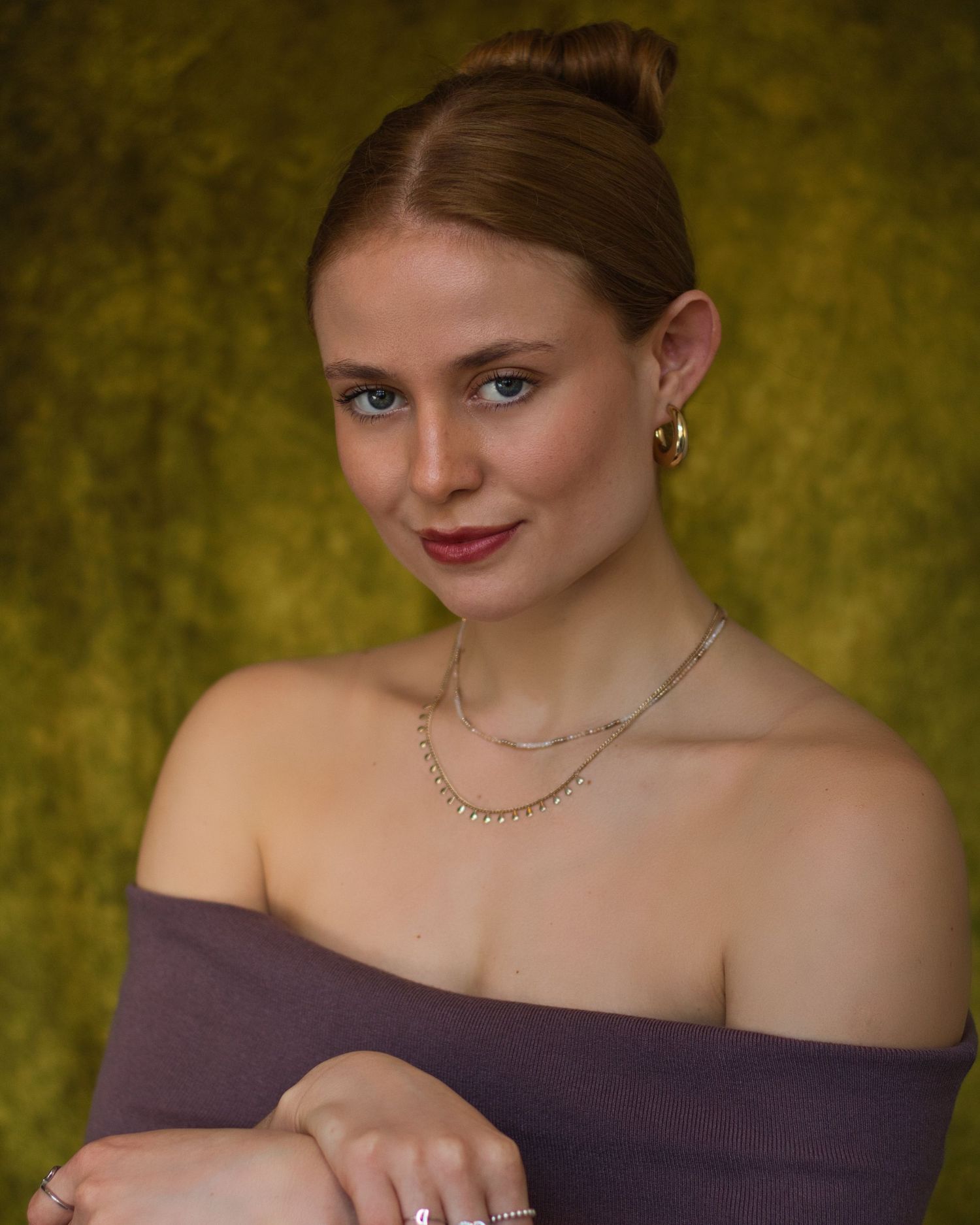 A woman in a brown off-shoulder top poses elegantly against a textured golden background.