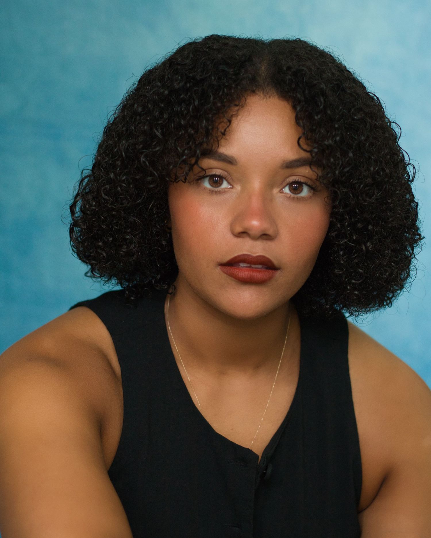 A portrait series showing a person with curly black hair and red lipstick against a blue background in various poses.